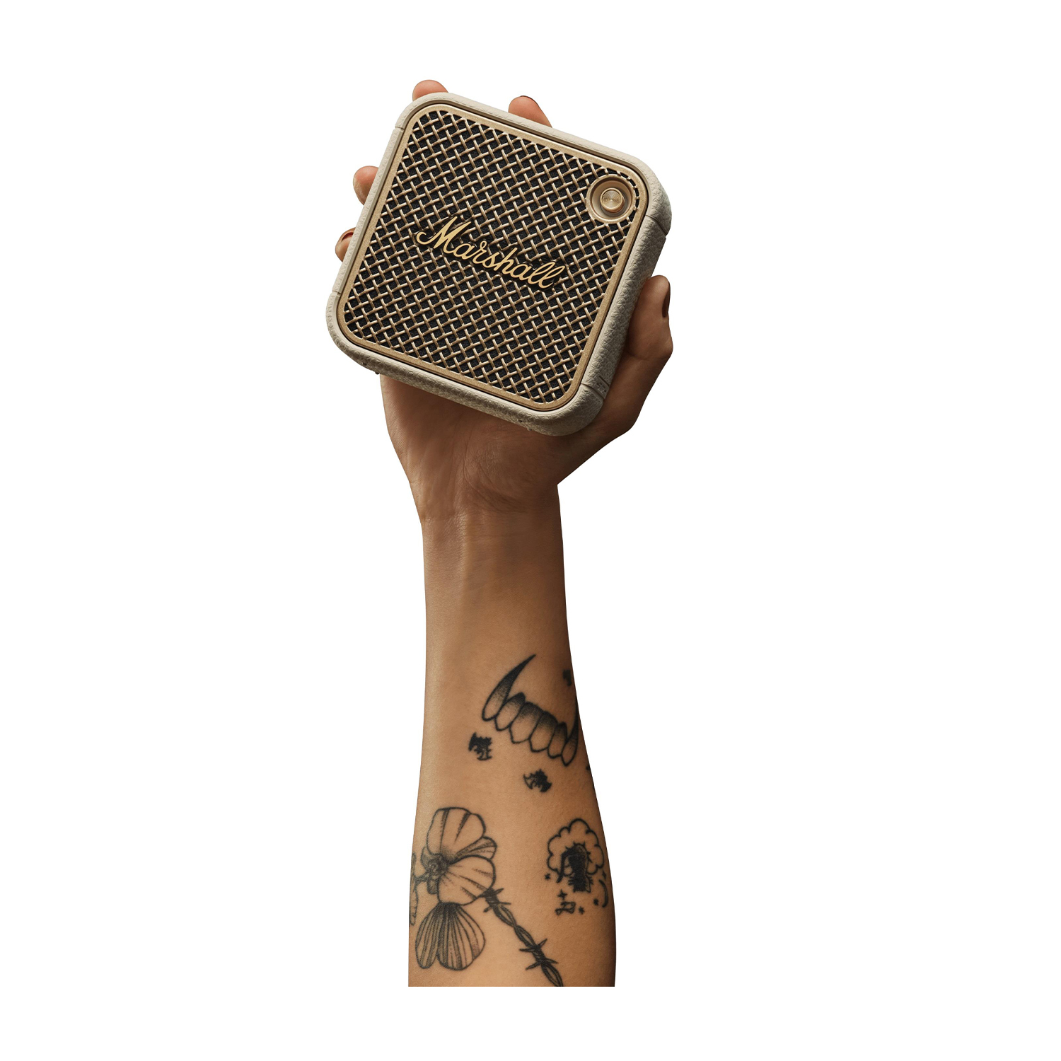 Una mano tiene in mano un piccolo altoparlante beige e oro con una parte anteriore in rete, tatuaggi sul braccio.