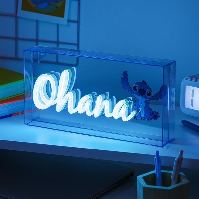 Kék fémdoboz 'Ohana' neonfelirattal. Jobbra Stitch rajzfilmfigura. Tollak és egy óra a közelben.