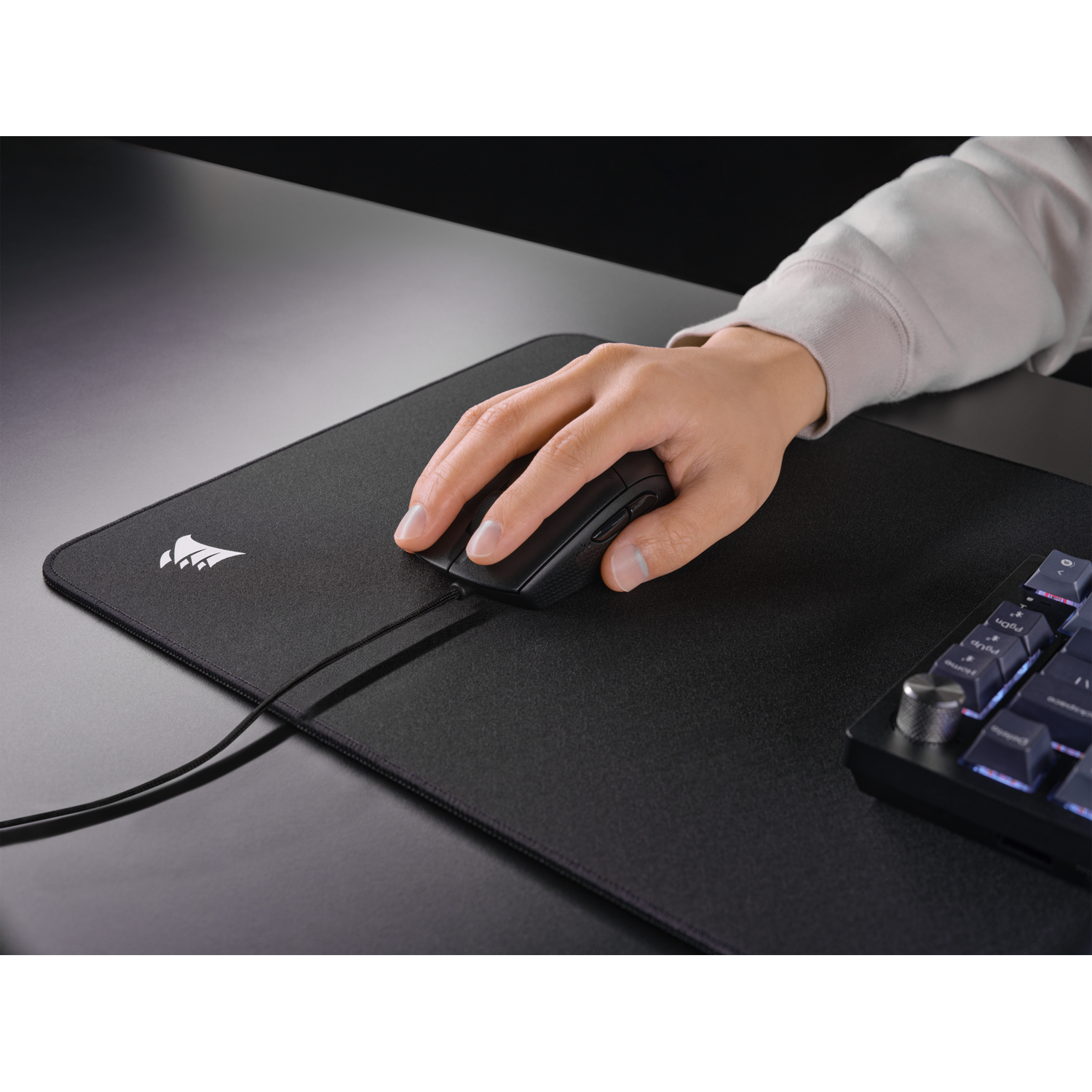 Person using a mouse on a black mousepad with a keyboard nearby.