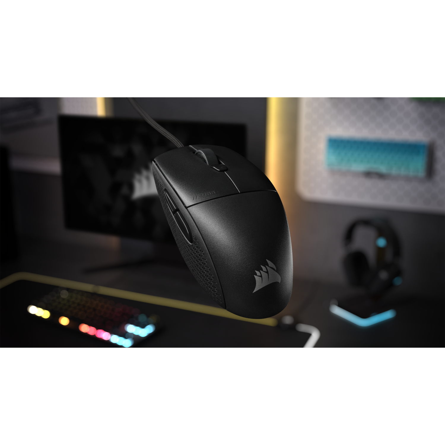 Black computer mouse on a desk. Corsair logo visible. Background includes monitor and headphones.