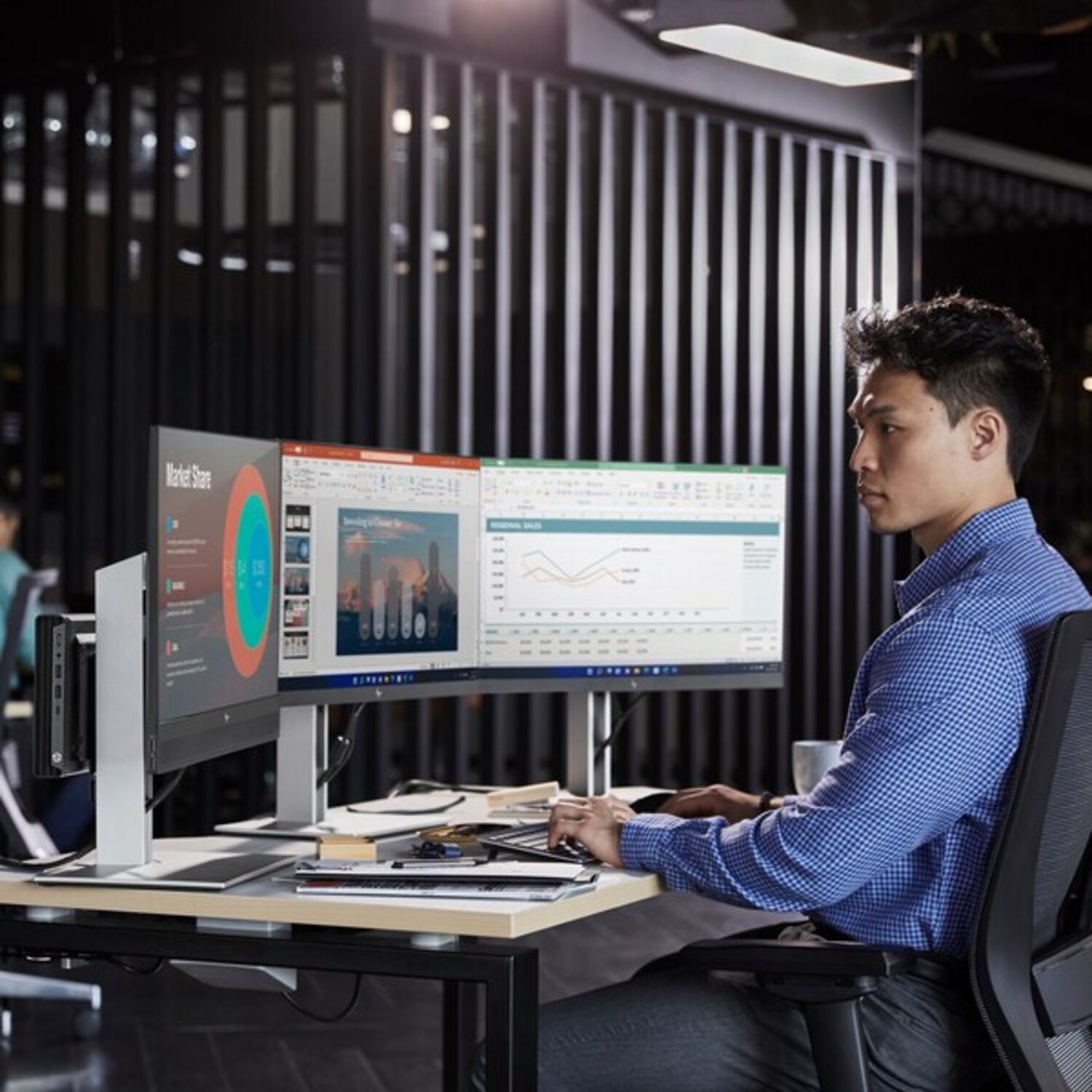 Een man die aan een bureau werkt met twee monitoren en een computer.