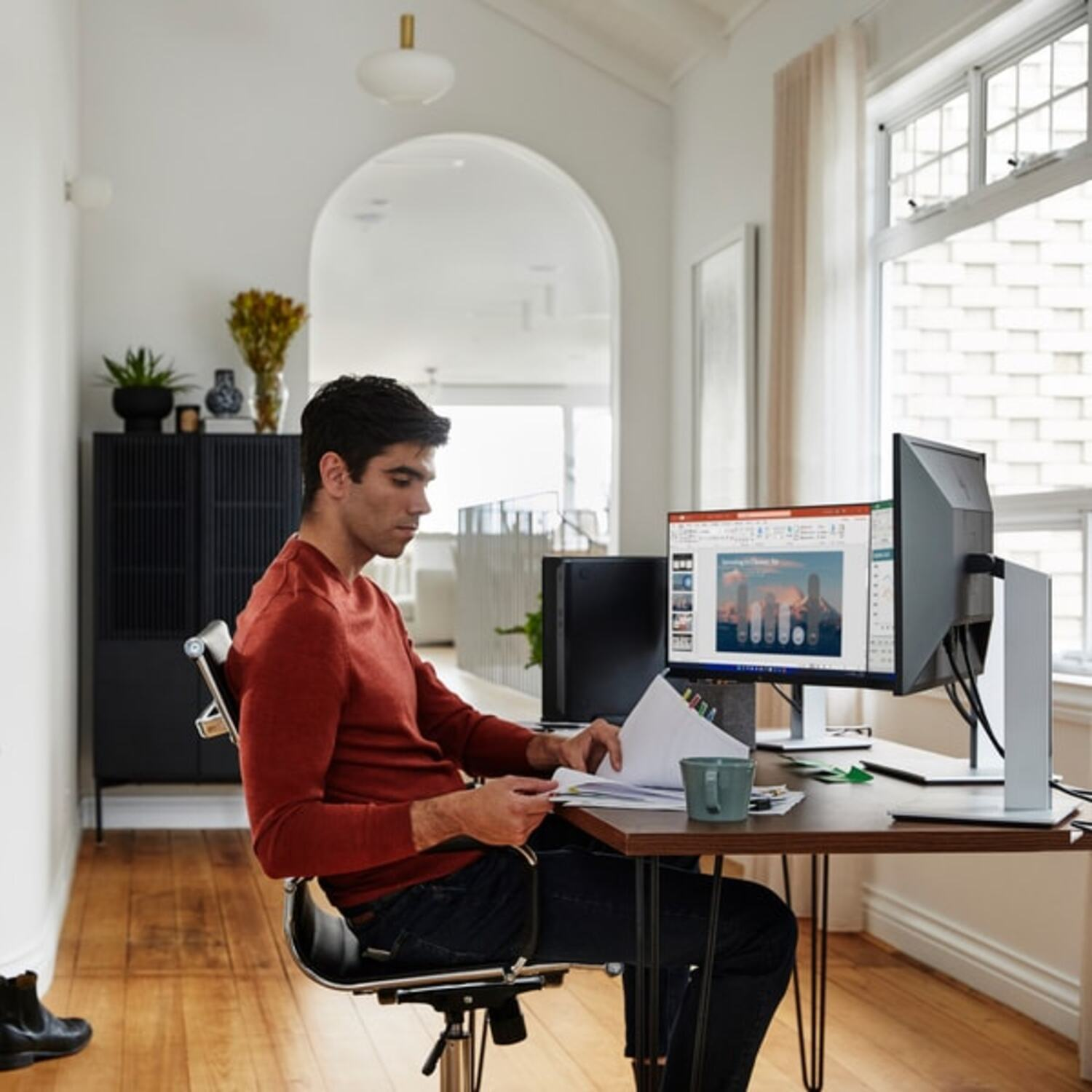 Man die werkt aan een bureau met twee monitoren, documenten en een mok.
