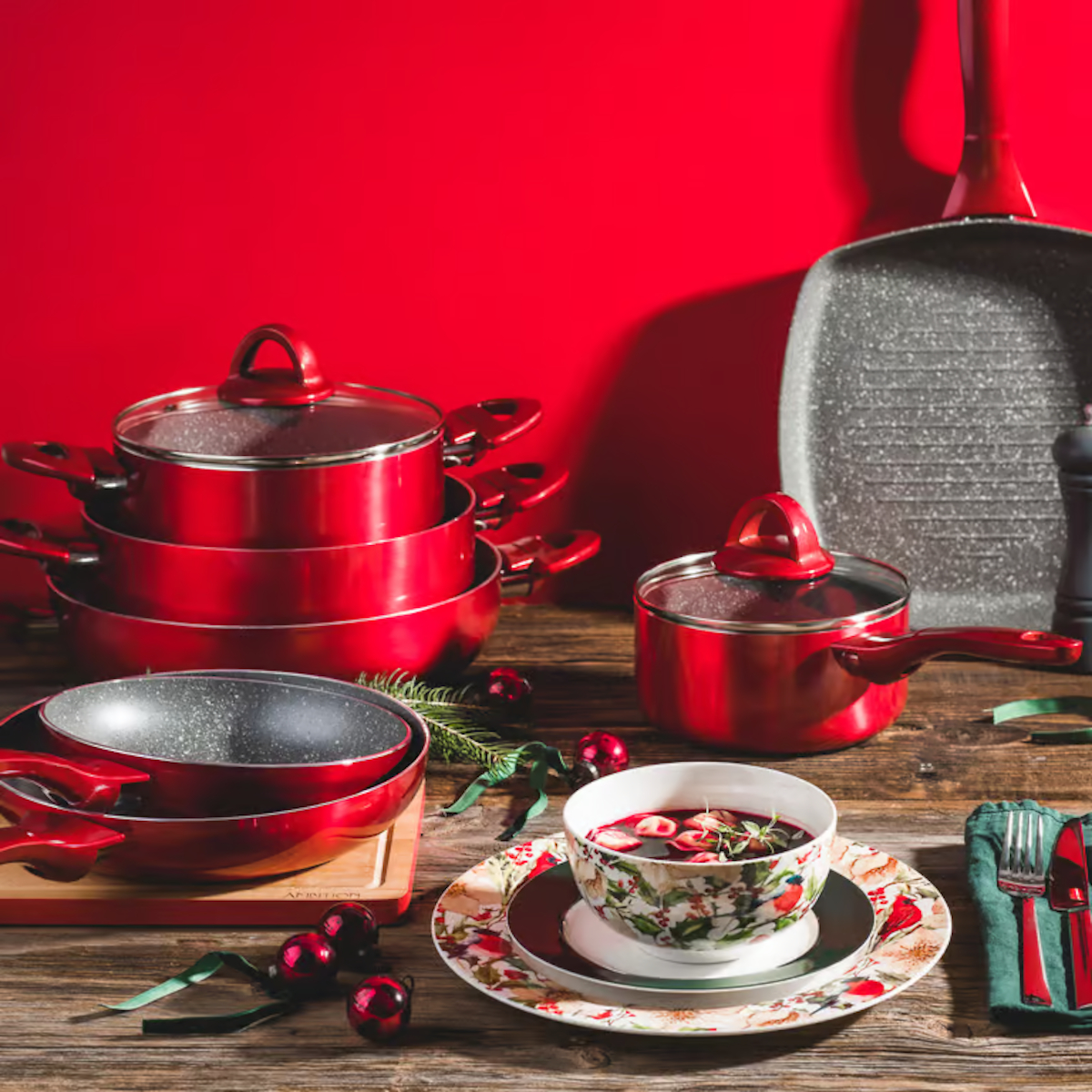 Świąteczna aranżacja z czerwonymi naczyniami kuchennymi i naczyniami. Zawiera miskę z zupą i patelnię.