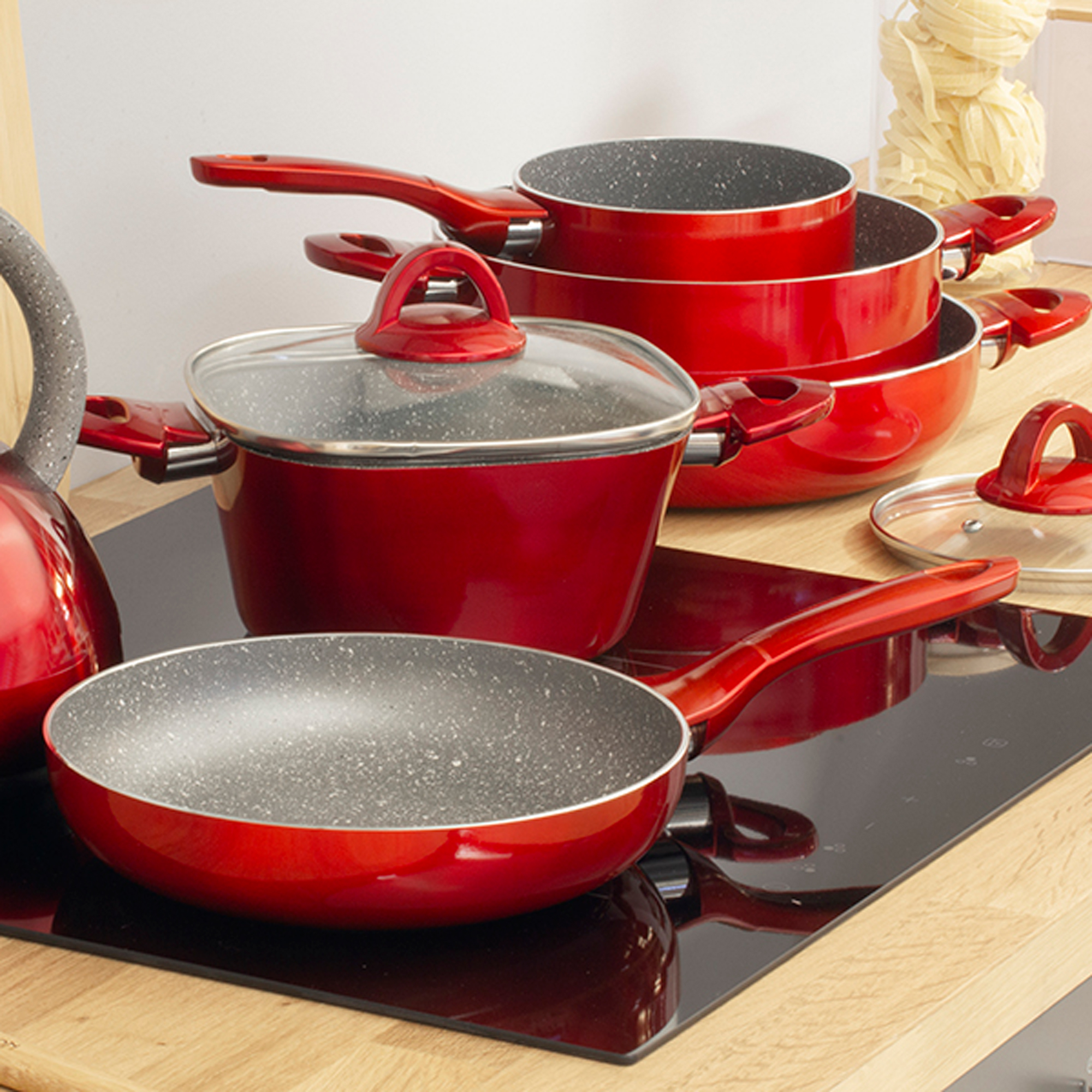 Zestaw czerwonych naczyń kuchennych na czarnej płycie grzewczej. Zestaw zawiera garnki, patelnie i pokrywki.