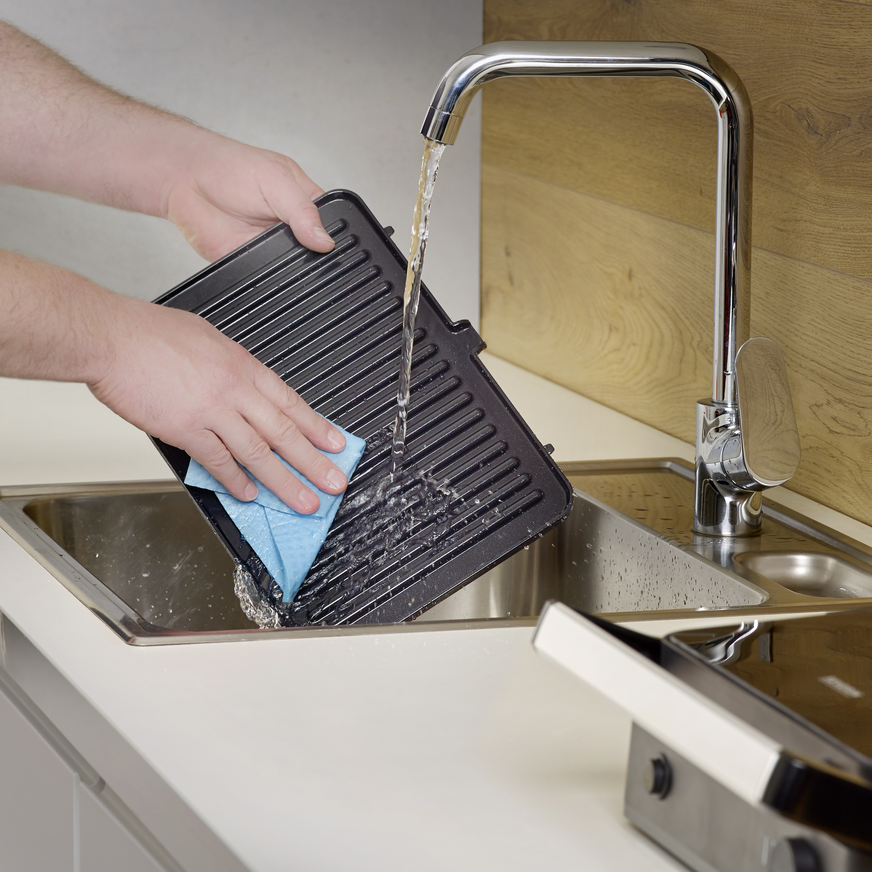 Person wäscht eine schwarze Grillpfanne in einem Waschbecken mit einem blauen Schwamm.