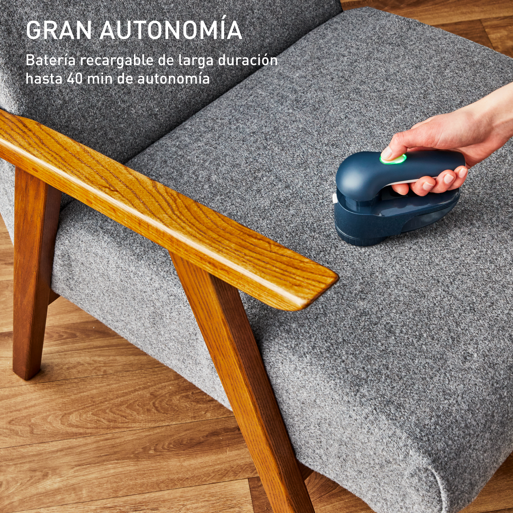 Una mano usando un quitapelusas en un sofá gris, con un reposabrazos de madera.