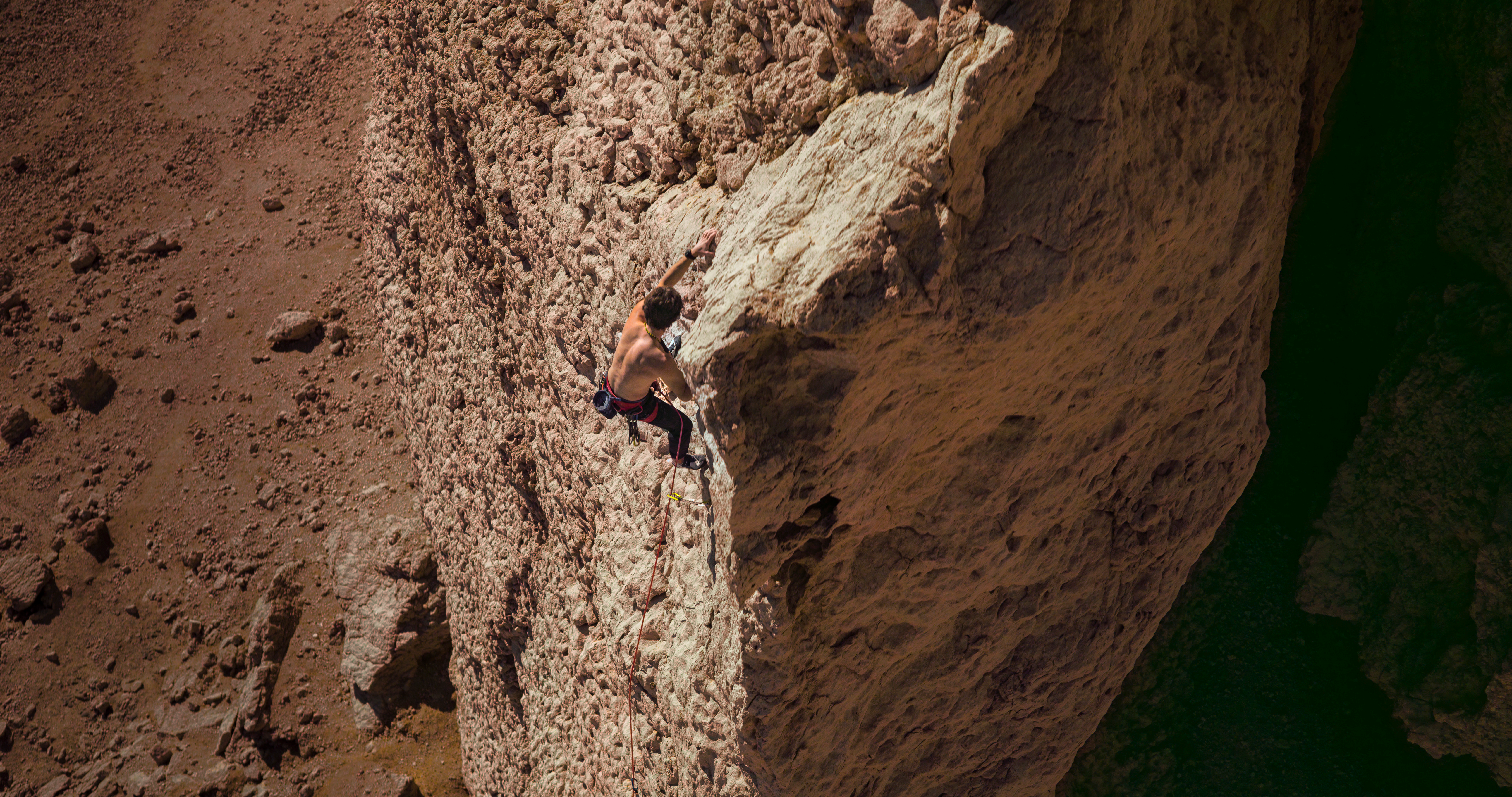Un alpinista che scala una parete rocciosa ripida con attrezzatura di sicurezza.
