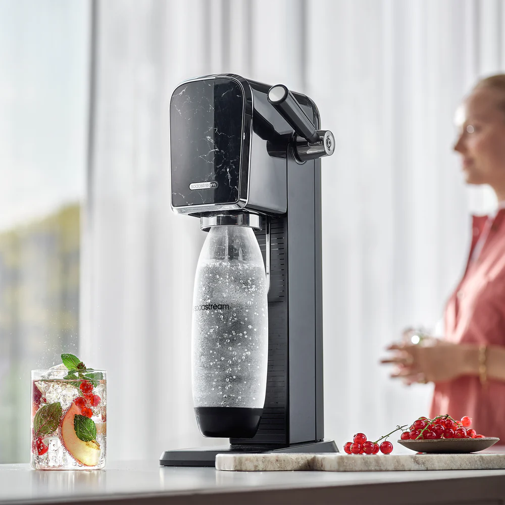 Machine à soda avec un verre de boisson aux fruits et à la glace. Une femme est en arrière-plan.