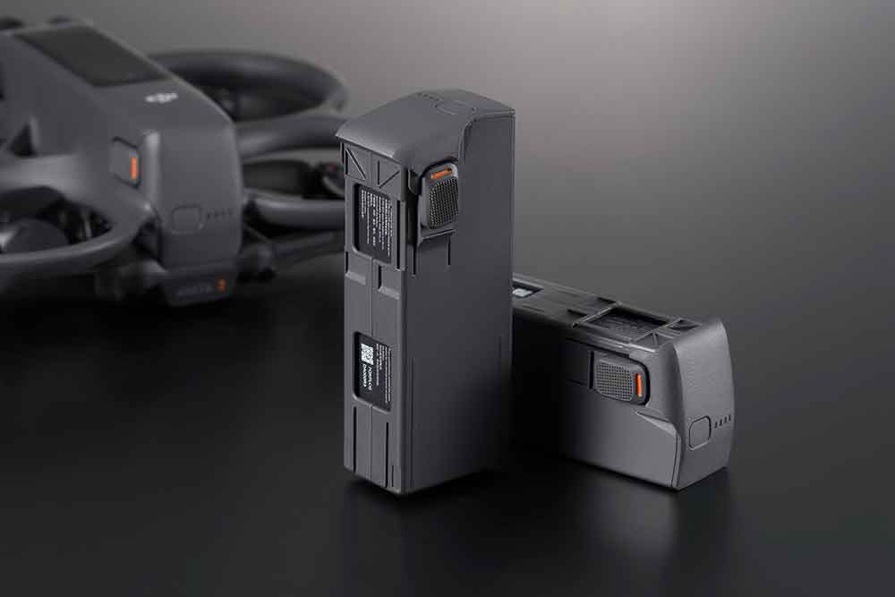 Two gray drone batteries. A drone is in the blurred background.