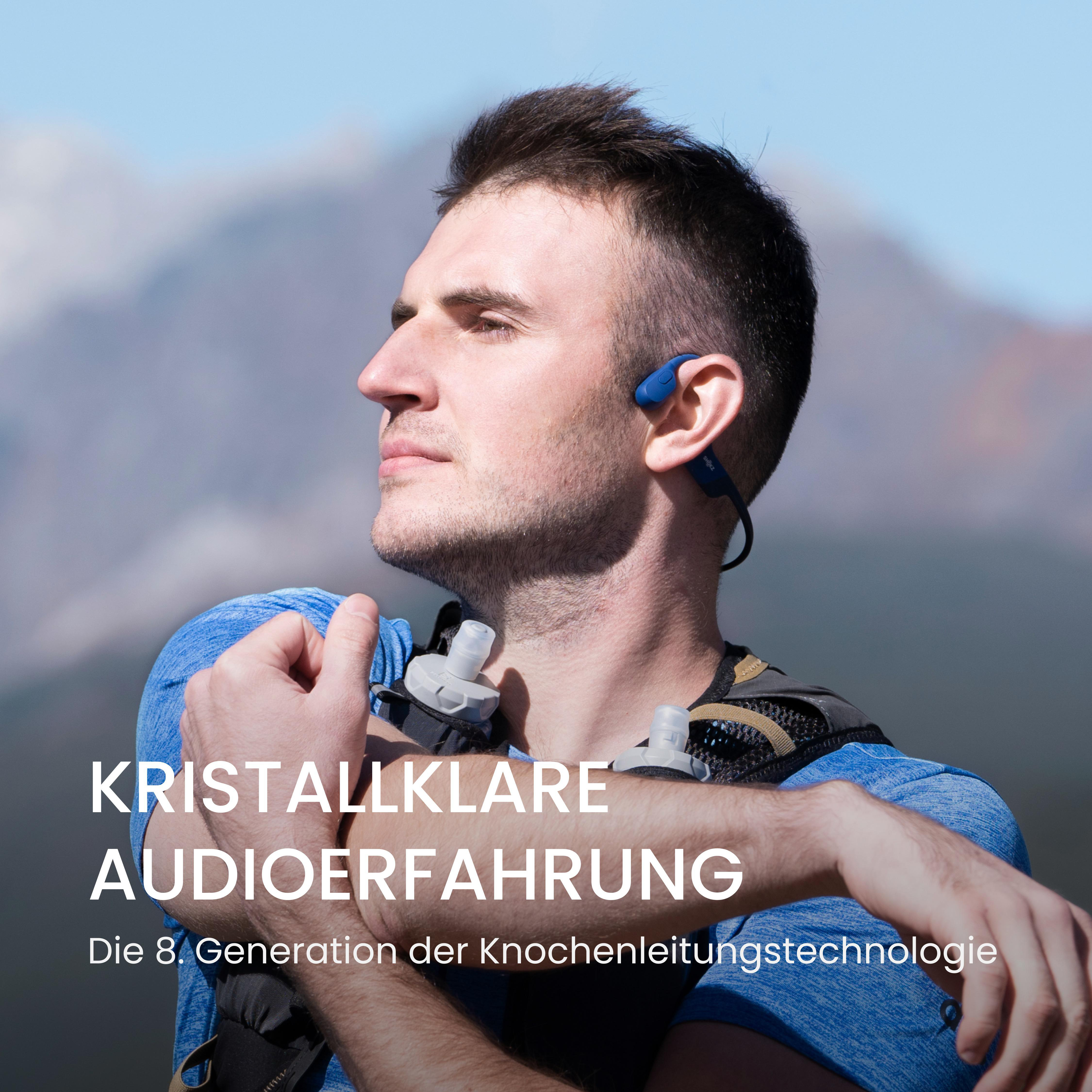 Ein Mann mit blauen Shokz-Kopfhörern. Er schaut nach oben und lächelt.
