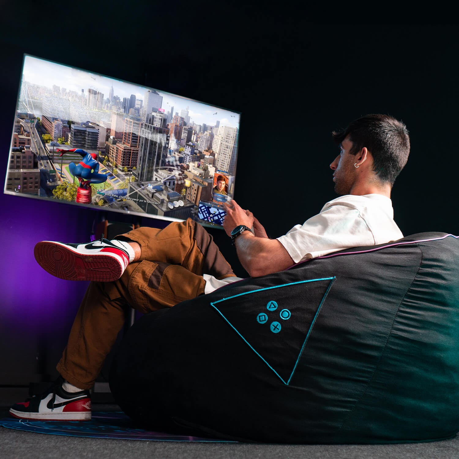 Hombre jugando videojuego en pantalla grande. Sentado en un puf.