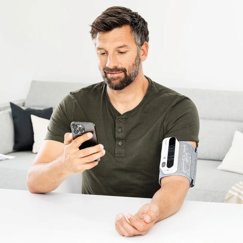 Homme utilisant un smartphone avec un tensiomètre au bras.