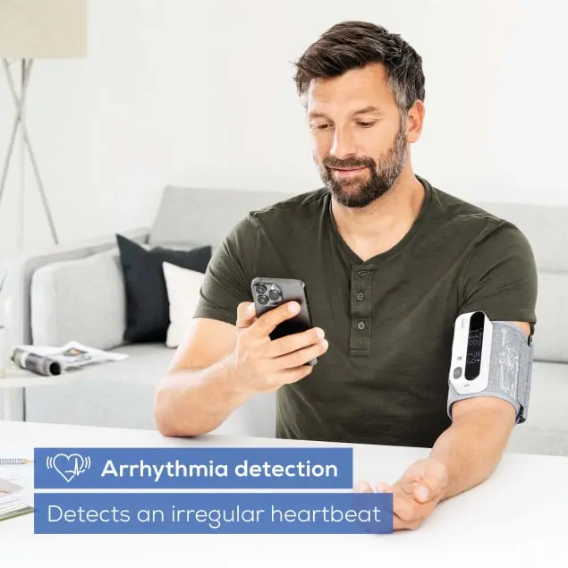 Homme utilisant un tensiomètre au bras, regardant un téléphone. Texte : Détection d'arythmie.
