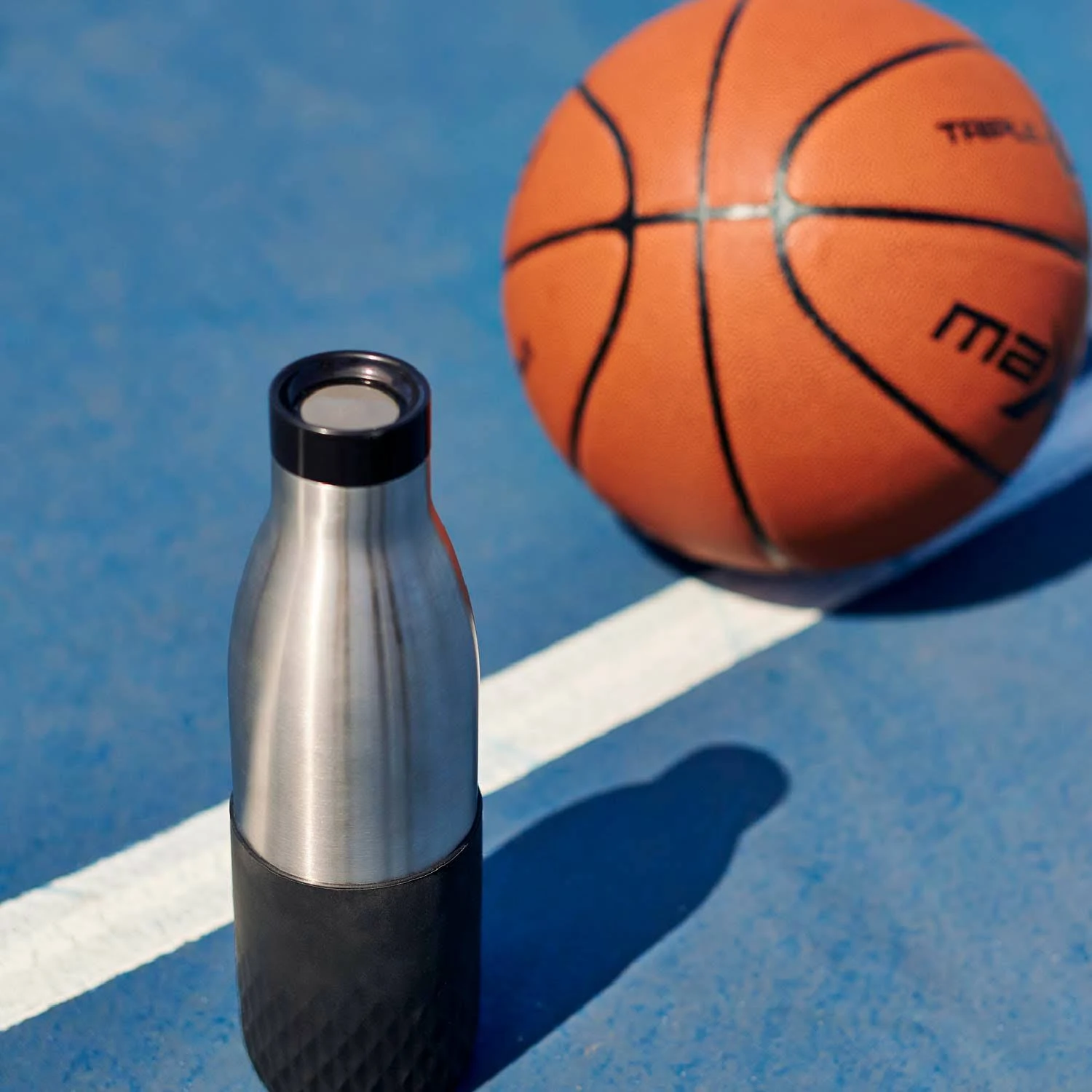 Una botella de agua de acero inoxidable y una pelota de baloncesto sobre una superficie azul.
