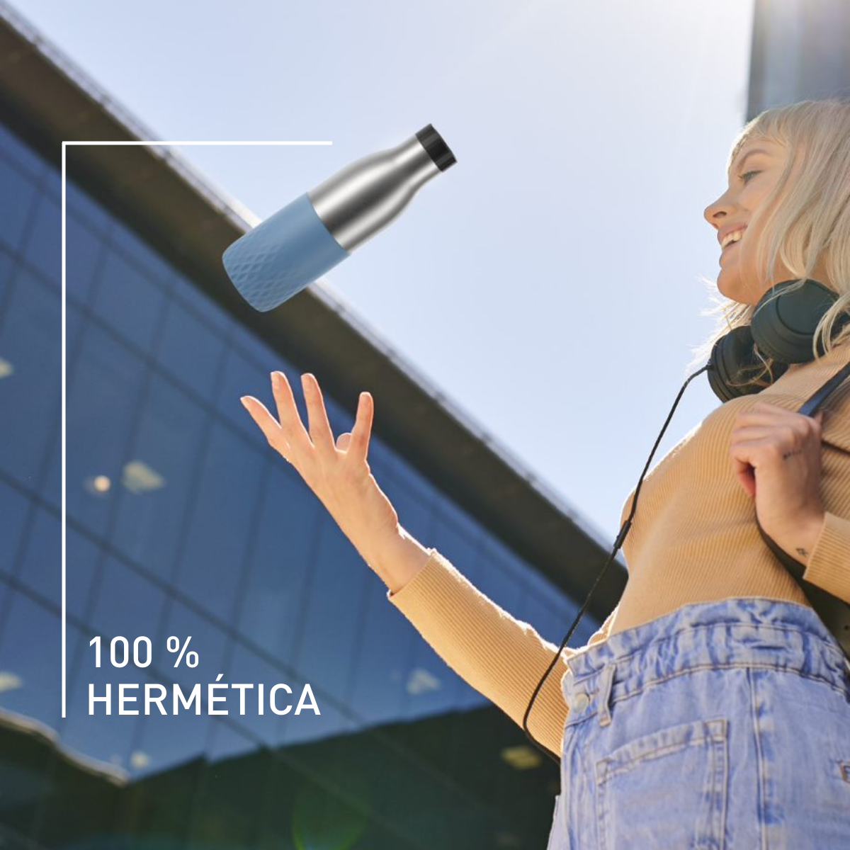 Mujer con auriculares, sosteniendo una botella de agua azul y plateada. Texto: 100% Hermética. Fondo soleado.