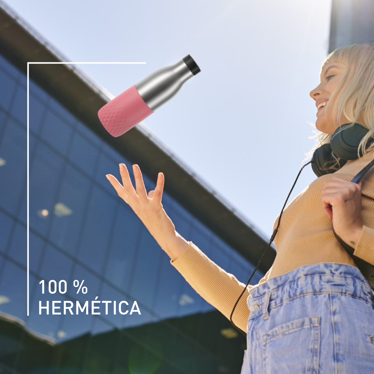 Una mujer lanza una botella rosa y plateada frente a un edificio.