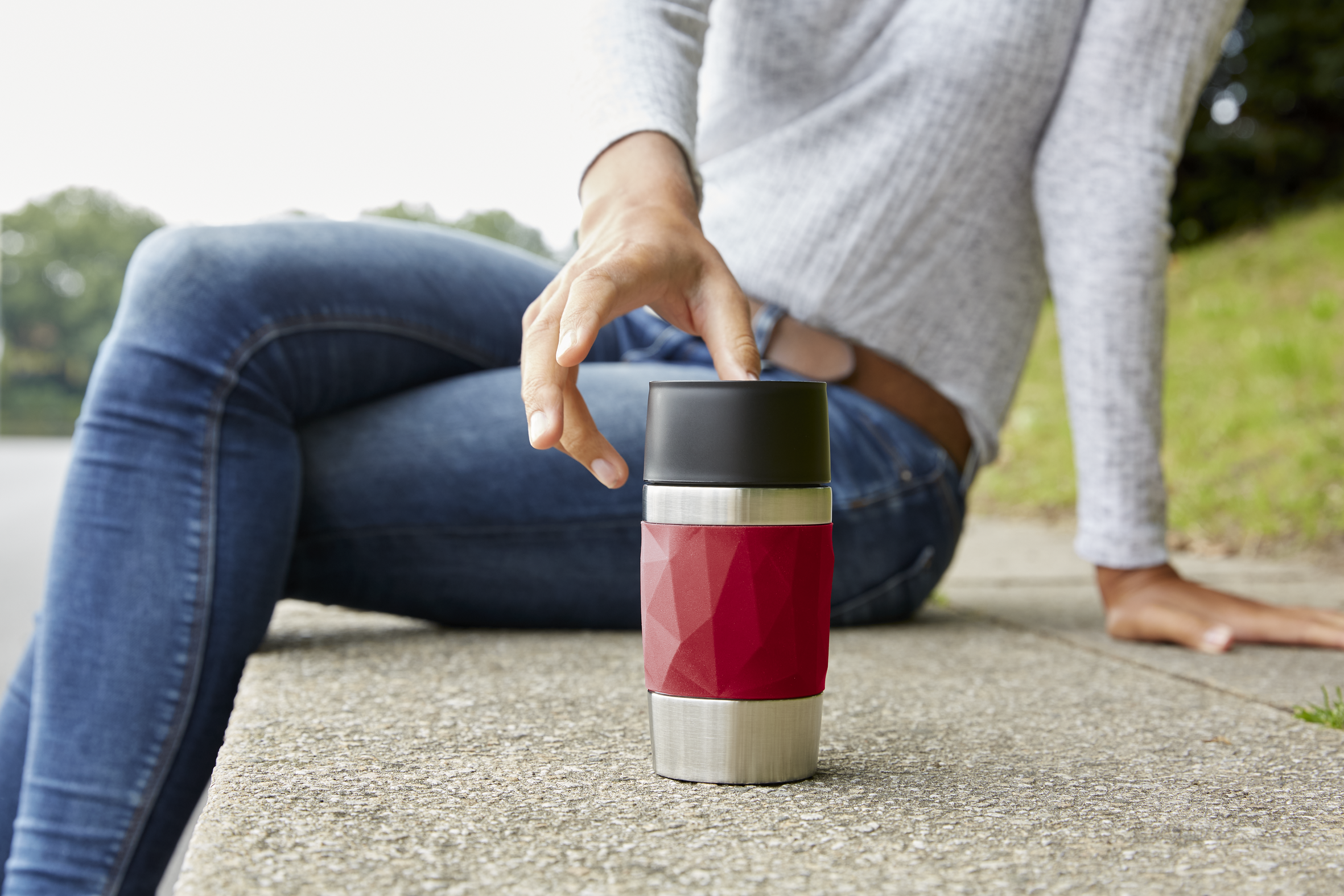 Persona sentada con un termo rojo y acero. Mano alcanza la taza.