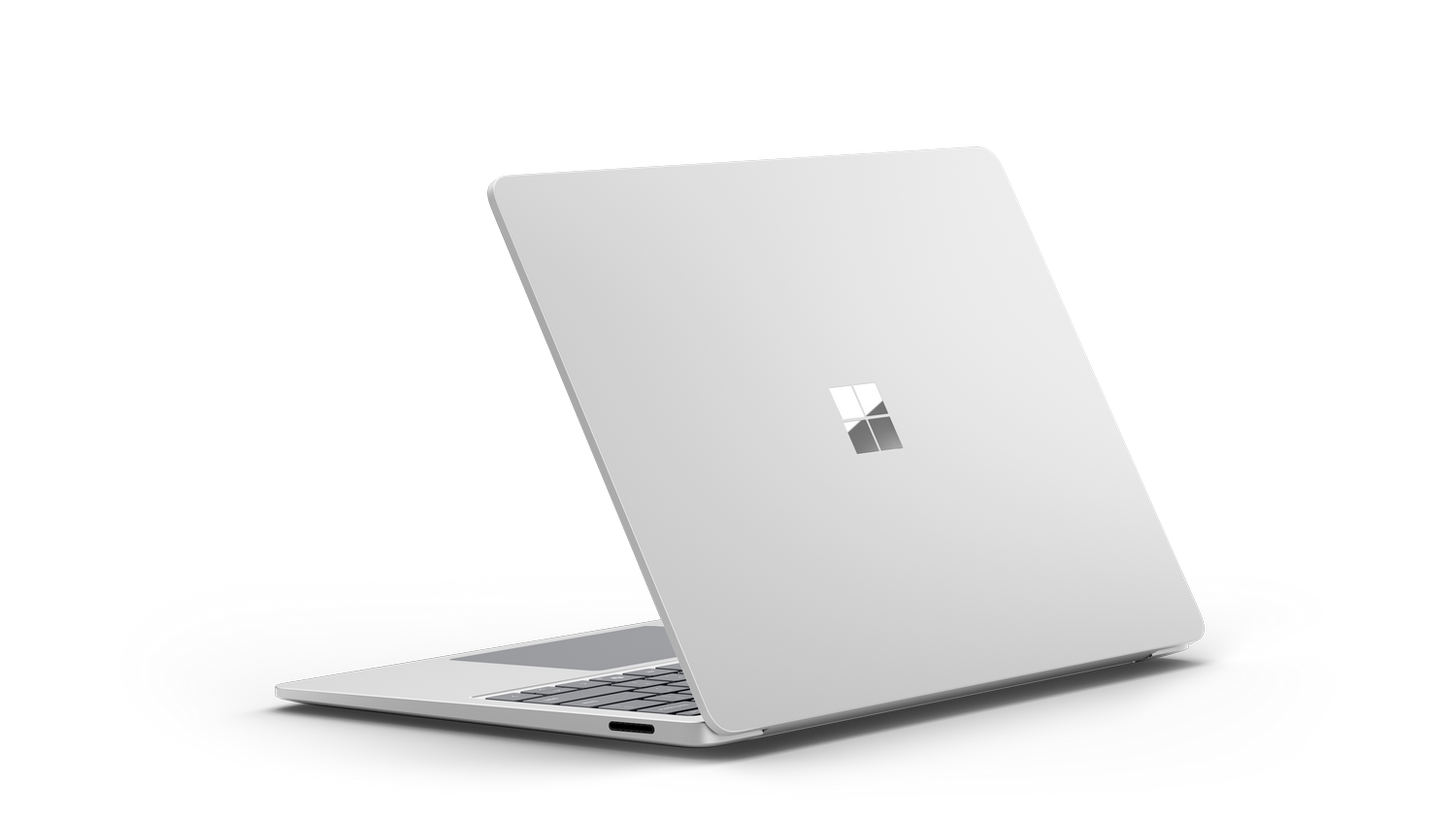 Un portátil plateado, en ángulo, con el logotipo de Microsoft en la parte trasera, sobre un fondo negro.