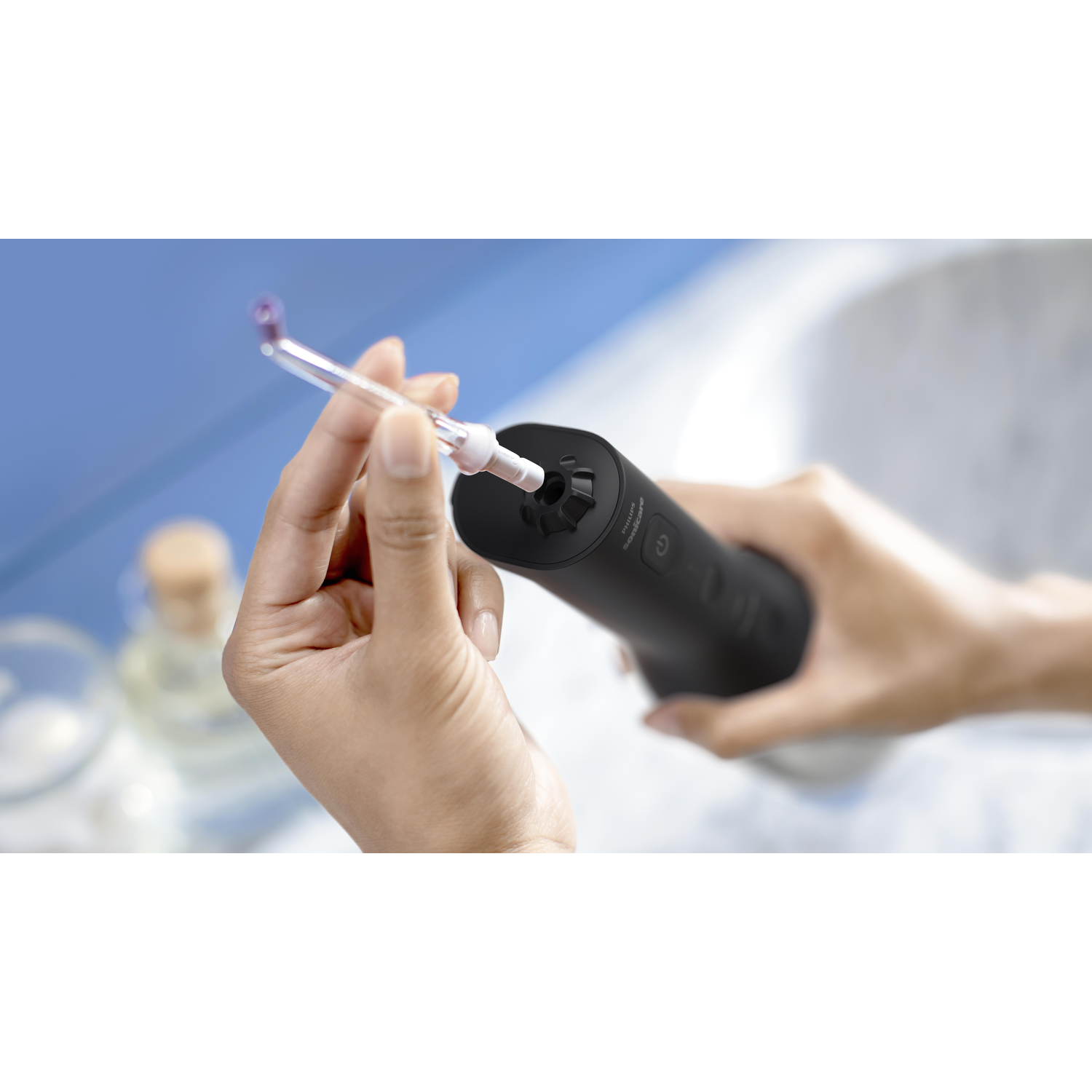 Person holding a black water flosser, inserting a cleaning tip. White background.