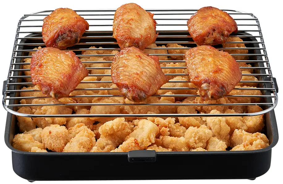 Ali di pollo su una griglia sopra pepite fritte in una padella nera.