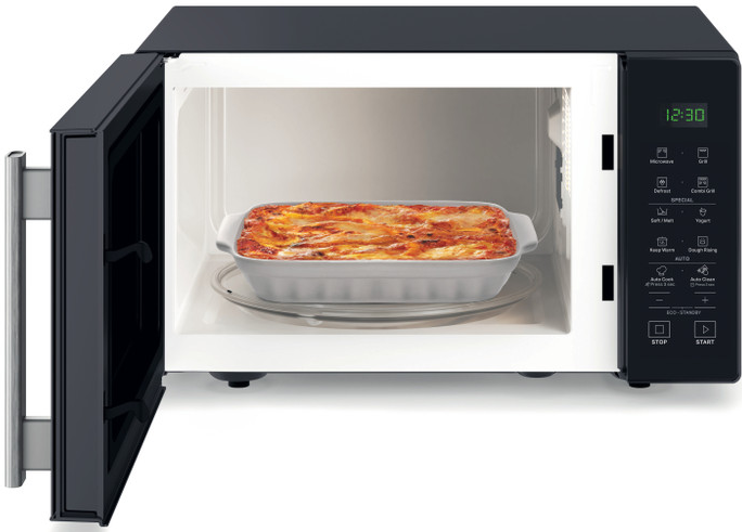 Un plat de lasagnes dans un plat blanc à l'intérieur d'un four à micro-ondes noir ouvert.