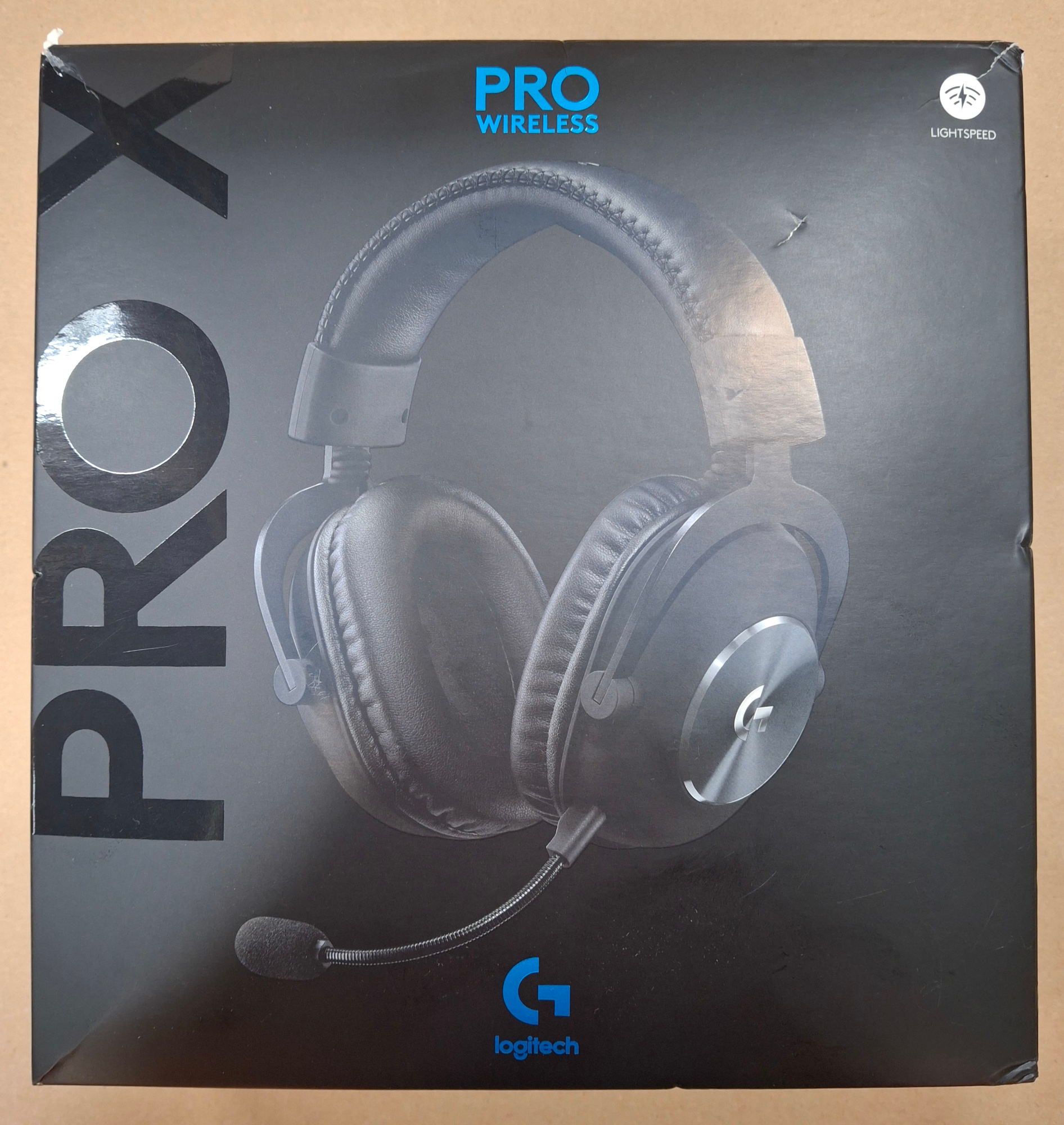 Pudełko na słuchawki, czarne z niebieskim napisem 'PRO WIRELESS'. Obraz słuchawek. Tło brązowe.