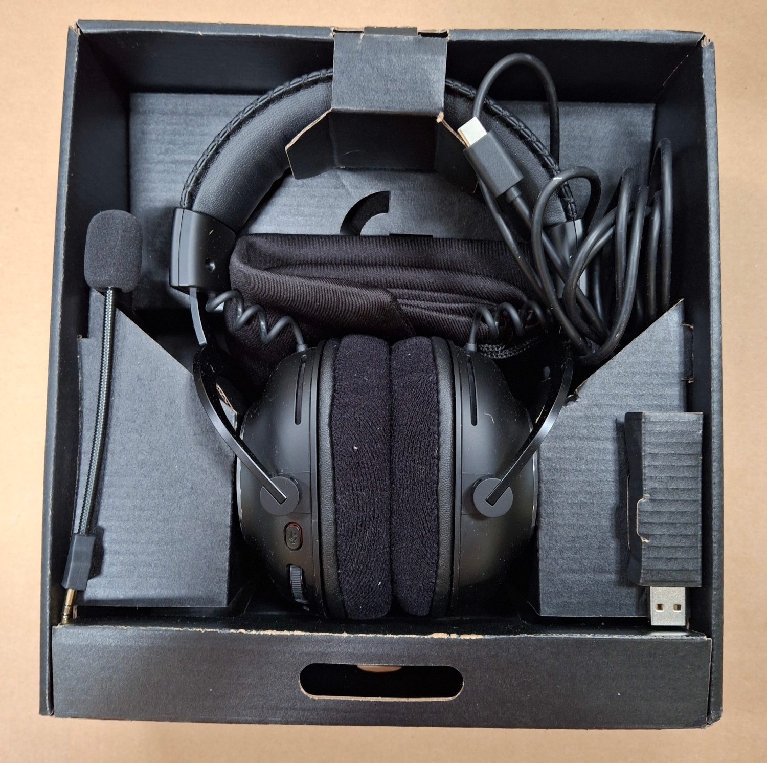Słuchawki w pudełku. Słuchawki są czarne, z mikrofonem i kluczem USB. Pudełko jest czarne.