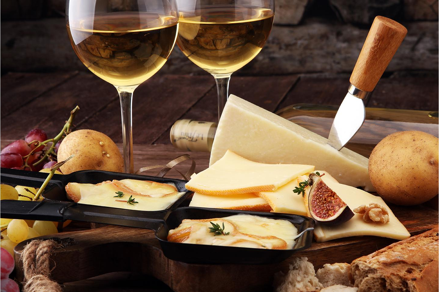 Formaggio e vino su un tavolo di legno. Include uva, fichi, pane e raclette.