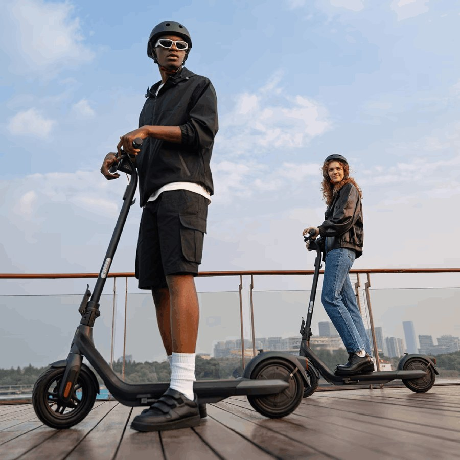 Dos personas en patinetes eléctricos. Uno es negro, con gafas de sol. El otro tiene rizos.