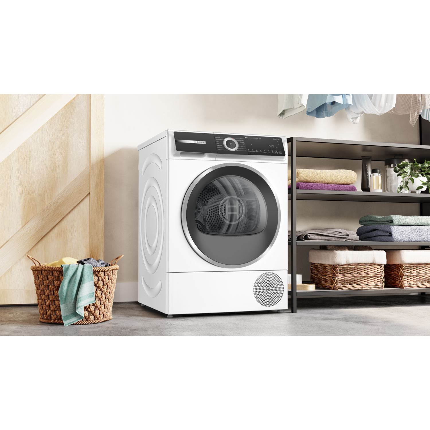 A white dryer next to a wooden door, a laundry basket, and a shelf with towels and plants.