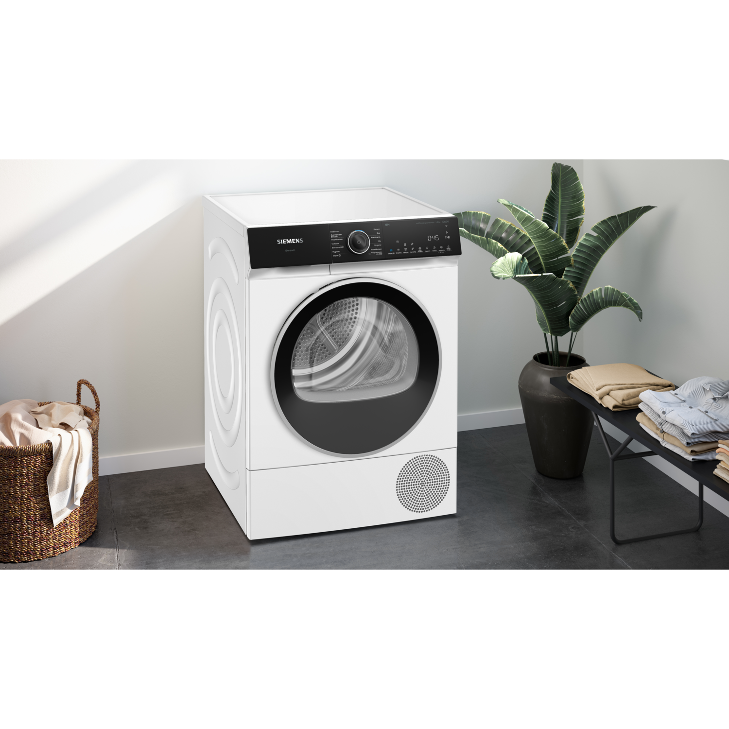 White Siemens dryer with basket and a plant, laundry on a table.