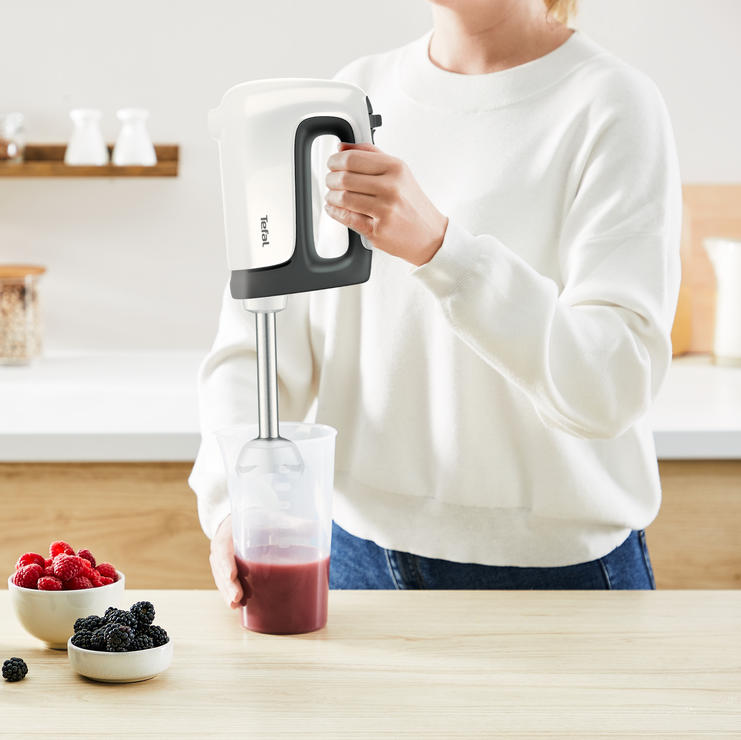 Eine Person, die einen weißen Stabmixer benutzt und rote Flüssigkeit in einem transparenten Behälter mischt.