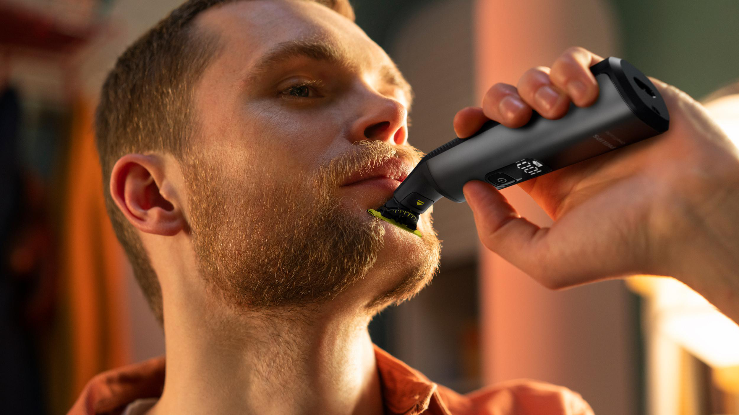 Ein Mann rasiert seinen Bart mit einem elektrischen Trimmer. Nahaufnahme, drinnen.