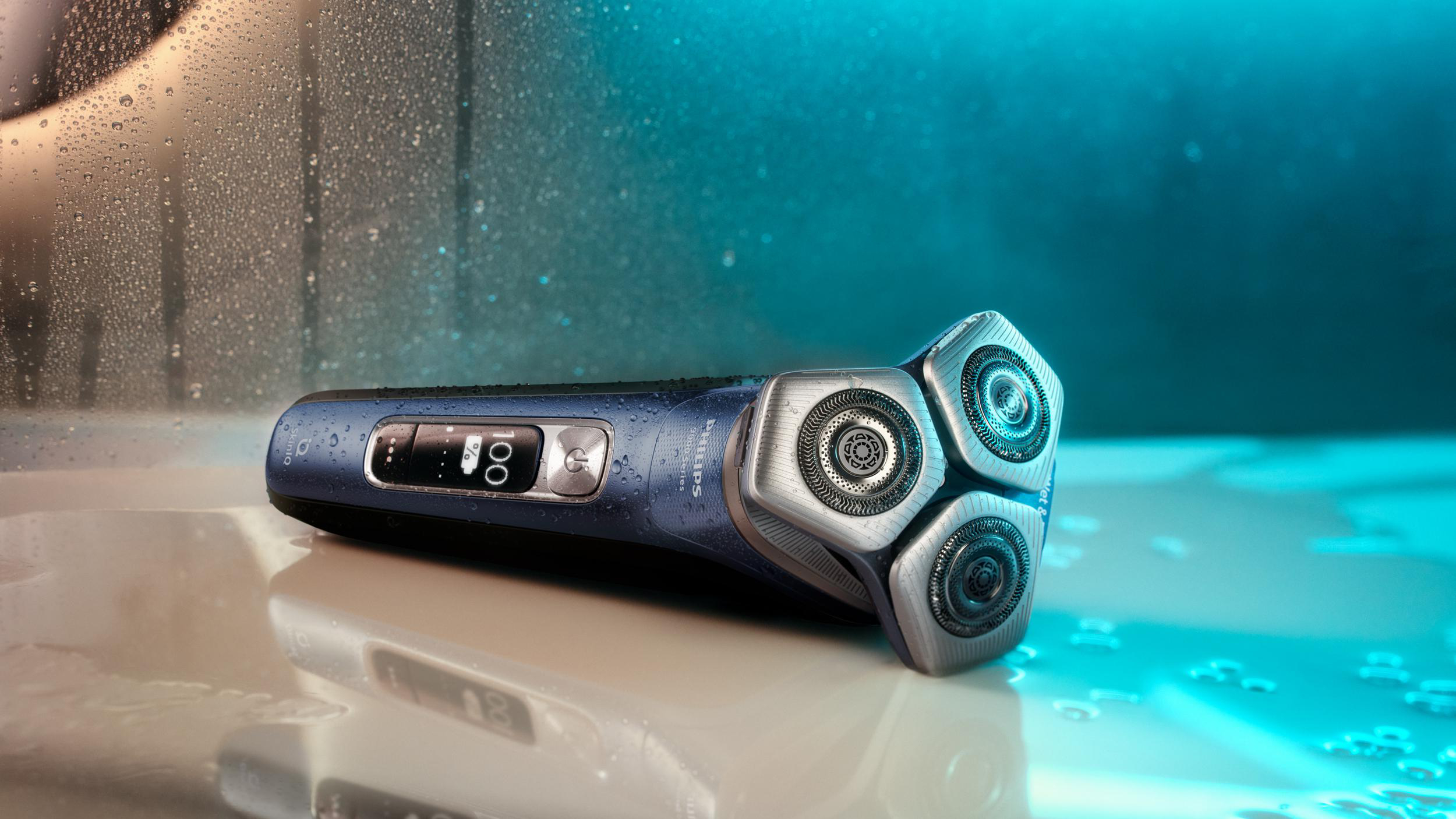 Nahaufnahme eines blau-silbernen Elektrorasierers, der auf einer nassen Oberfläche mit Wassertropfen liegt.