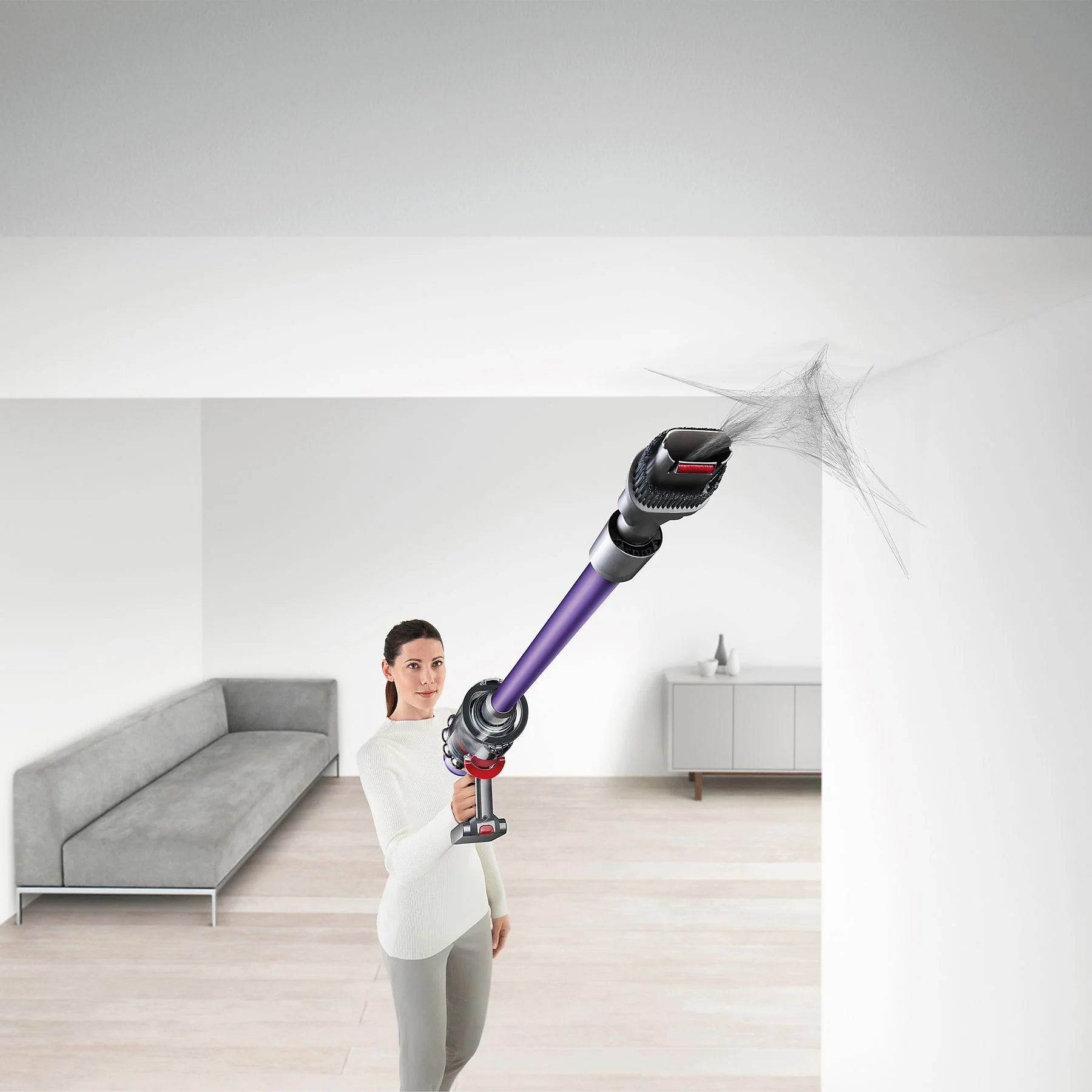 Une femme utilise un aspirateur violet et noir pour nettoyer un plafond blanc.