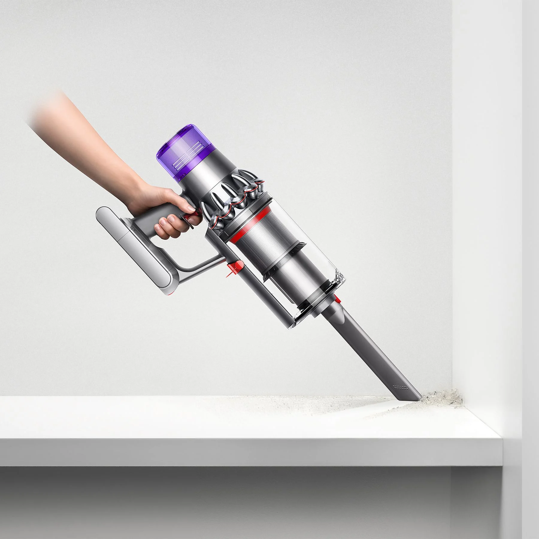 Main utilisant un aspirateur argent et violet sur une étagère blanche, enlevant la saleté.