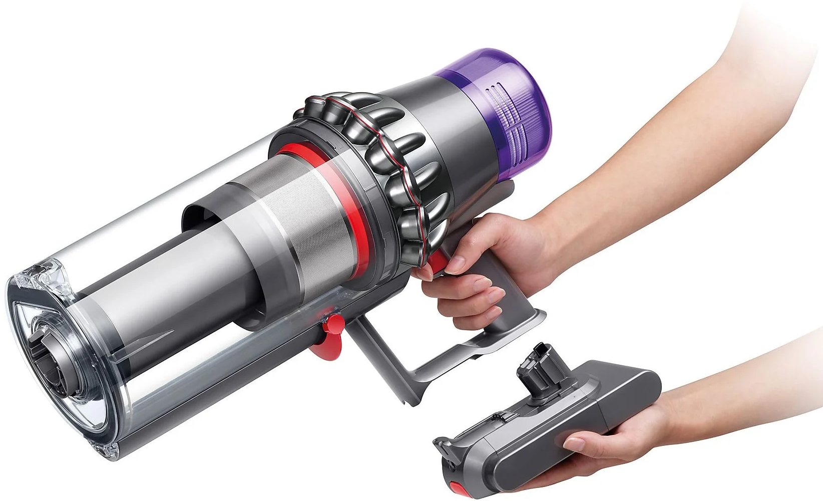 Un aspirateur Dyson argenté et noir tenu par deux mains. Un accessoire est à côté.