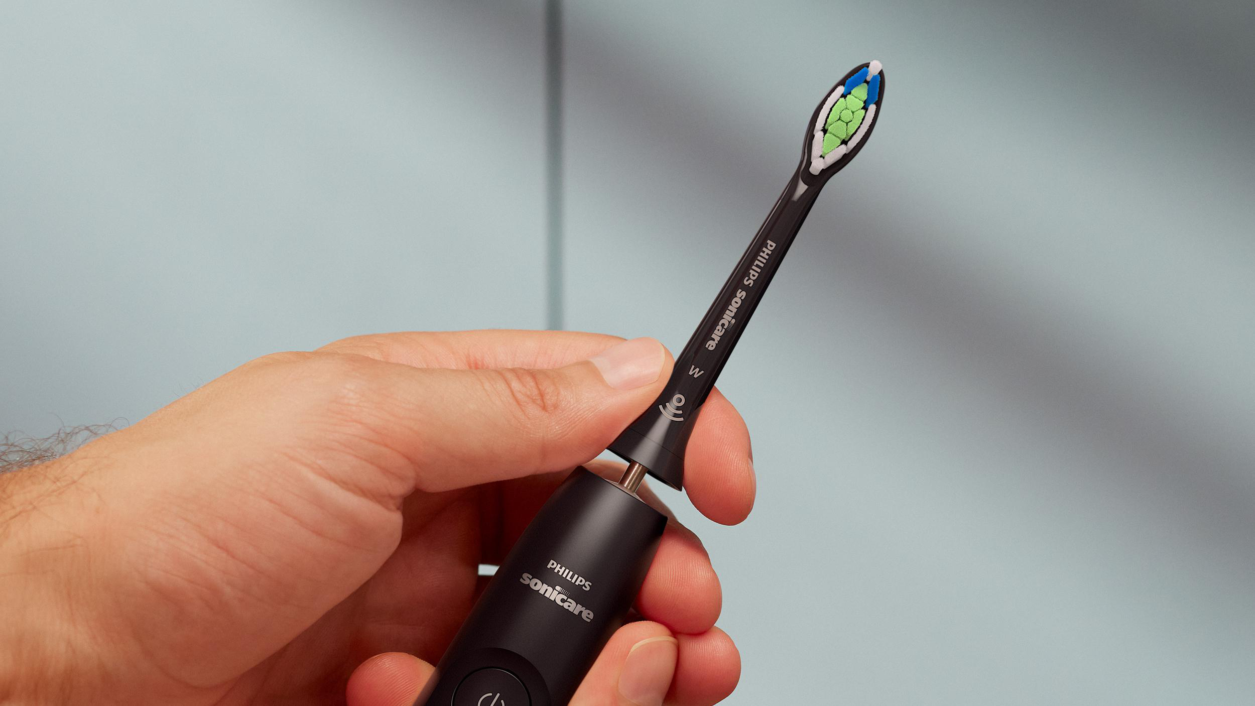 Eine Hand hält eine schwarze Philips Sonicare Zahnbürste. Der Bürstenkopf hat grüne und blaue Borsten.