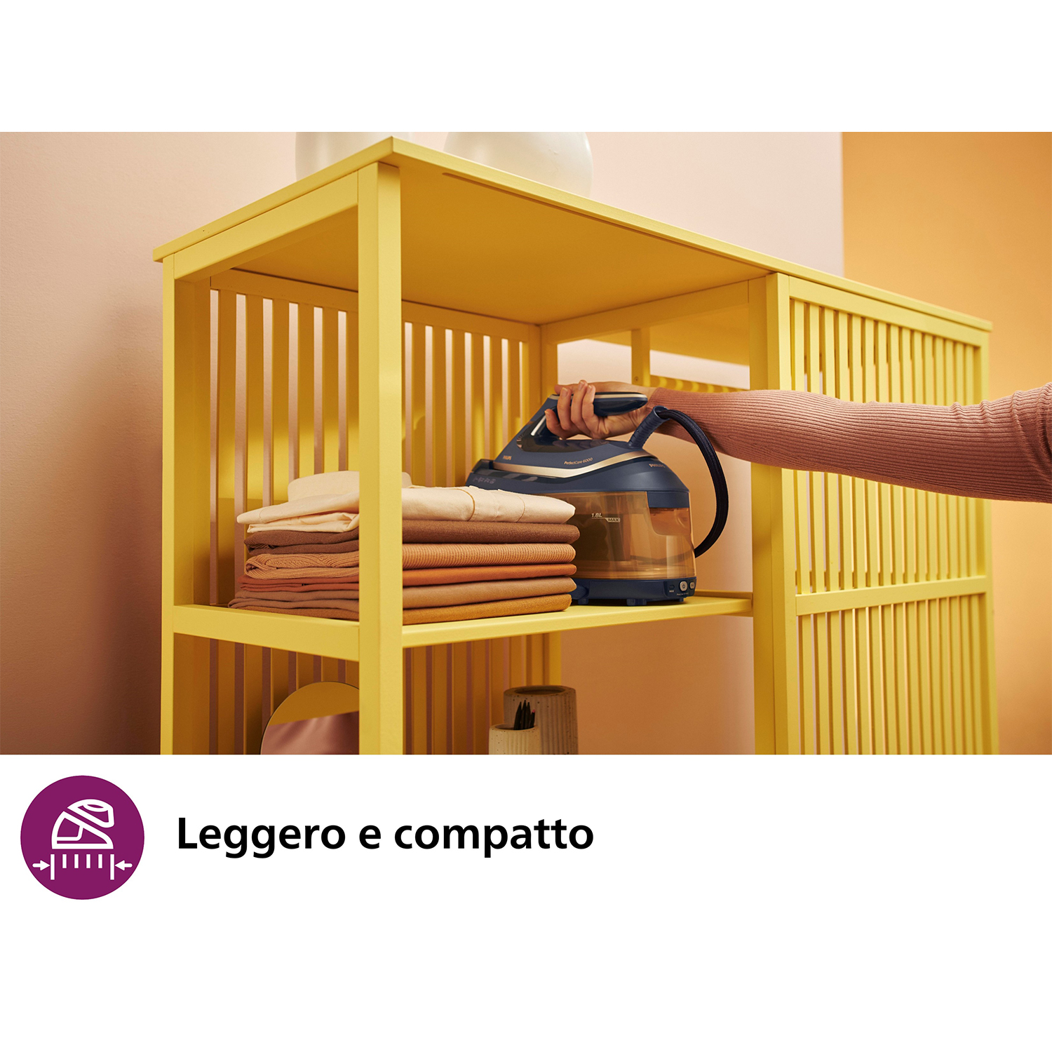 Una mensola gialla con un ferro da stiro blu e nero. Una mano lo afferra.