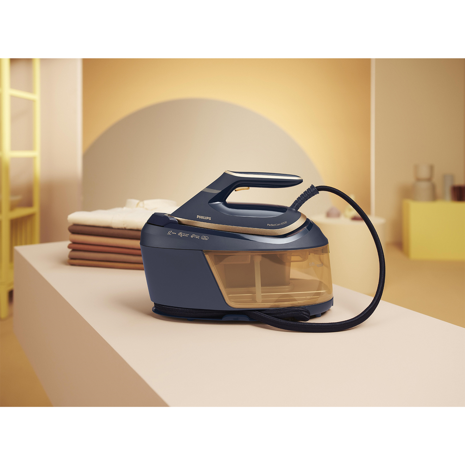 Un ferro da stiro a vapore blu navy e oro su una superficie beige con vestiti sullo sfondo.