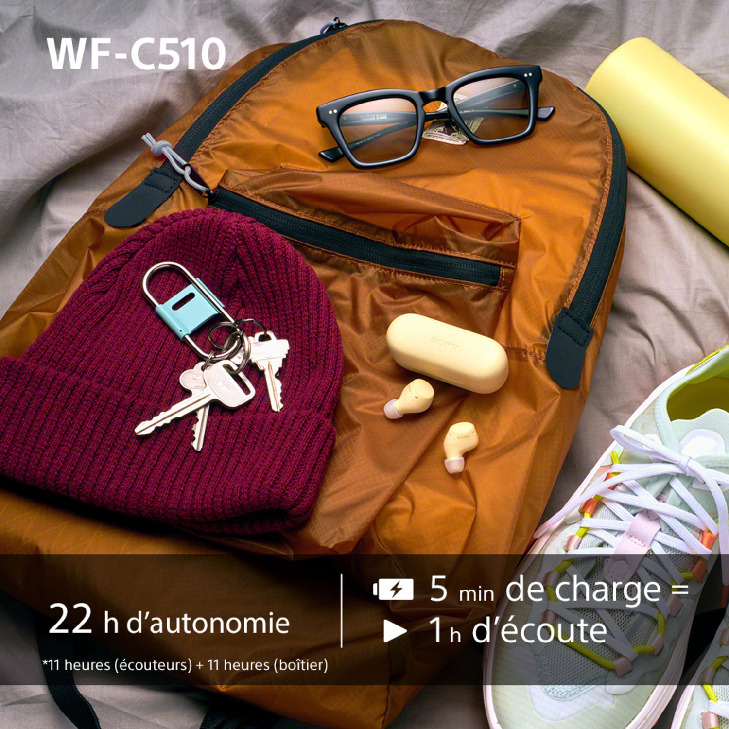 Sac à dos, lunettes, écouteurs, clés et chapeau sur un lit.