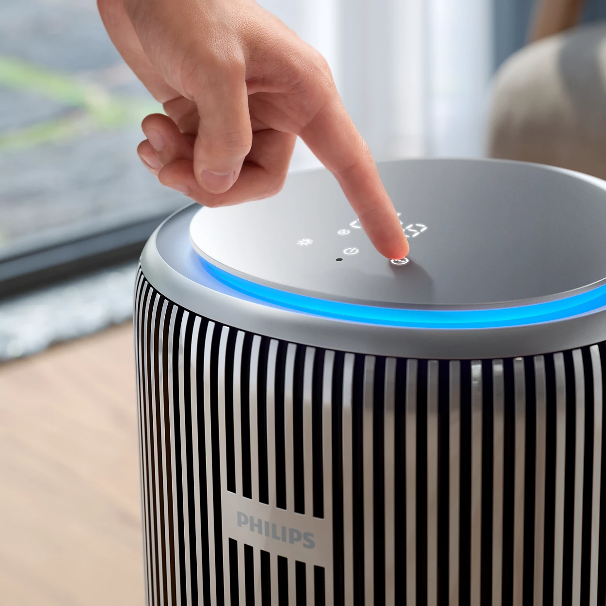 Egy személy ujja egy fekete-ezüst légtisztító gombját nyomja. A 'PHILIPS' logó látható.