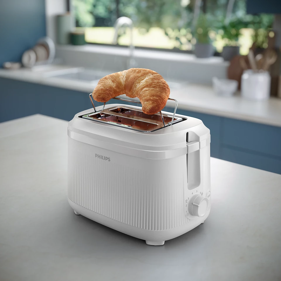 Egy fehér Philips kenyérpirító egy croissant-val a tetején. Konyha enteriőr a háttérben.