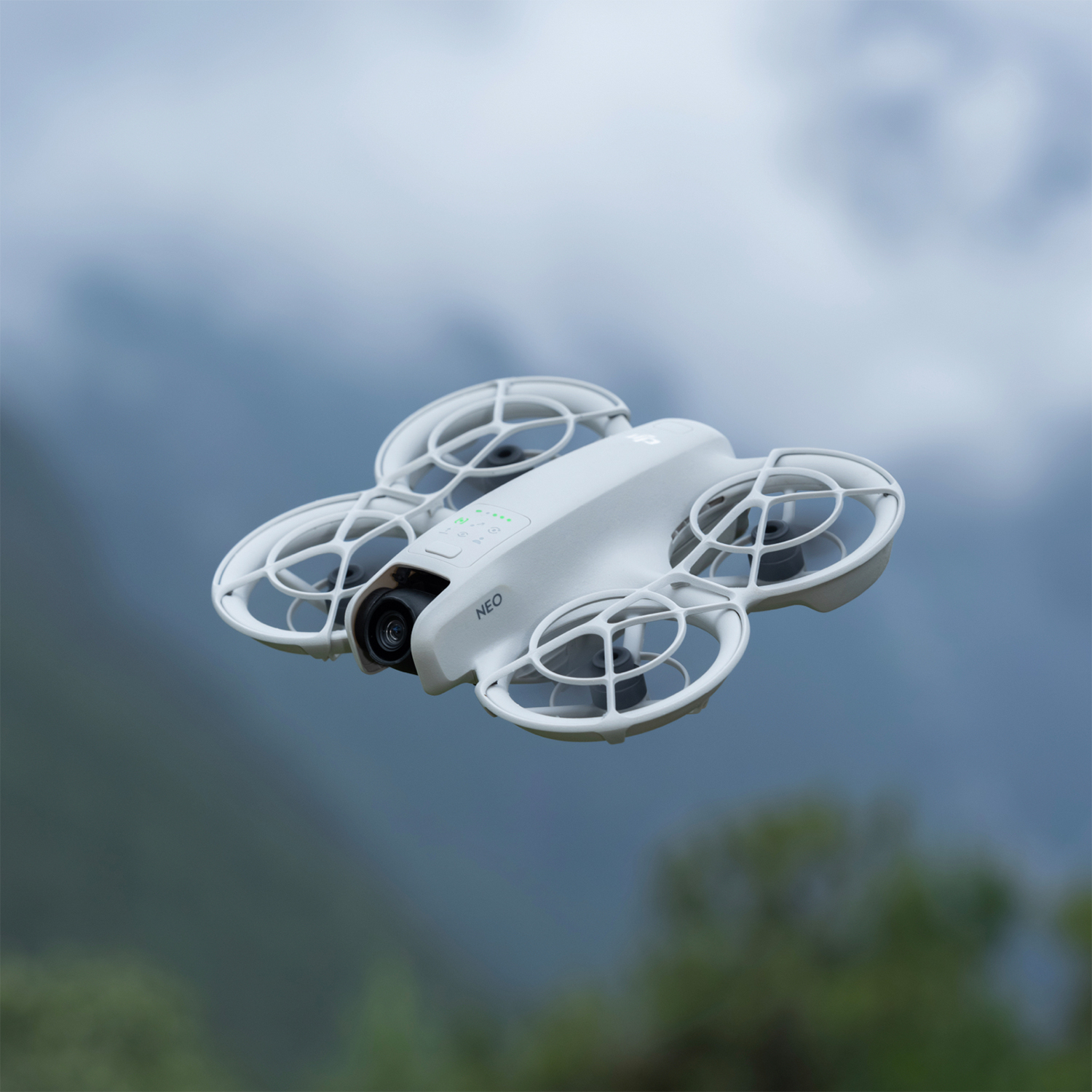 Un drone bianco con quattro eliche in volo, sfondo sfocato verde e blu.