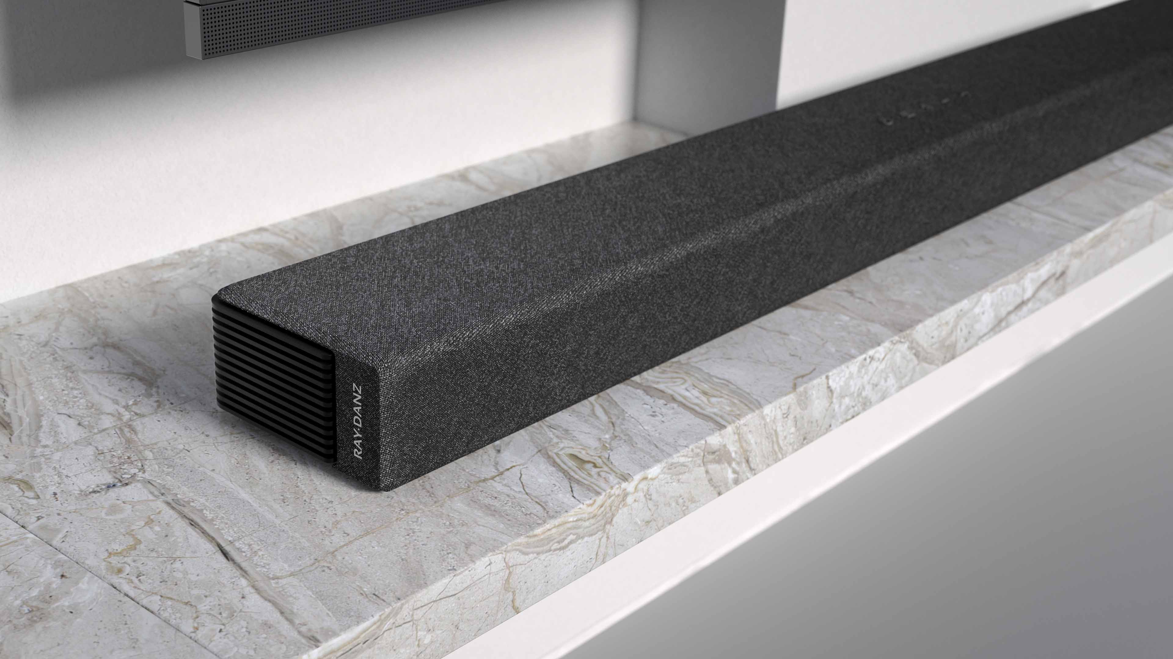 Mermer bir yüzeyde siyah bir soundbar, bir televizyonun bulunduğu bir duvara yakın.