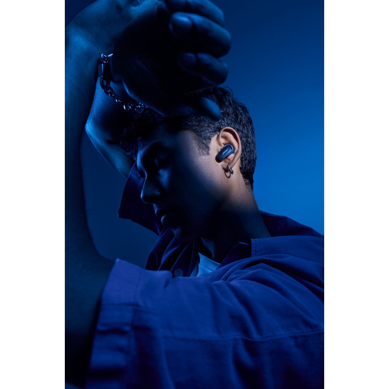 Man with earbud in ear, lights and shadows, dark blue environment.