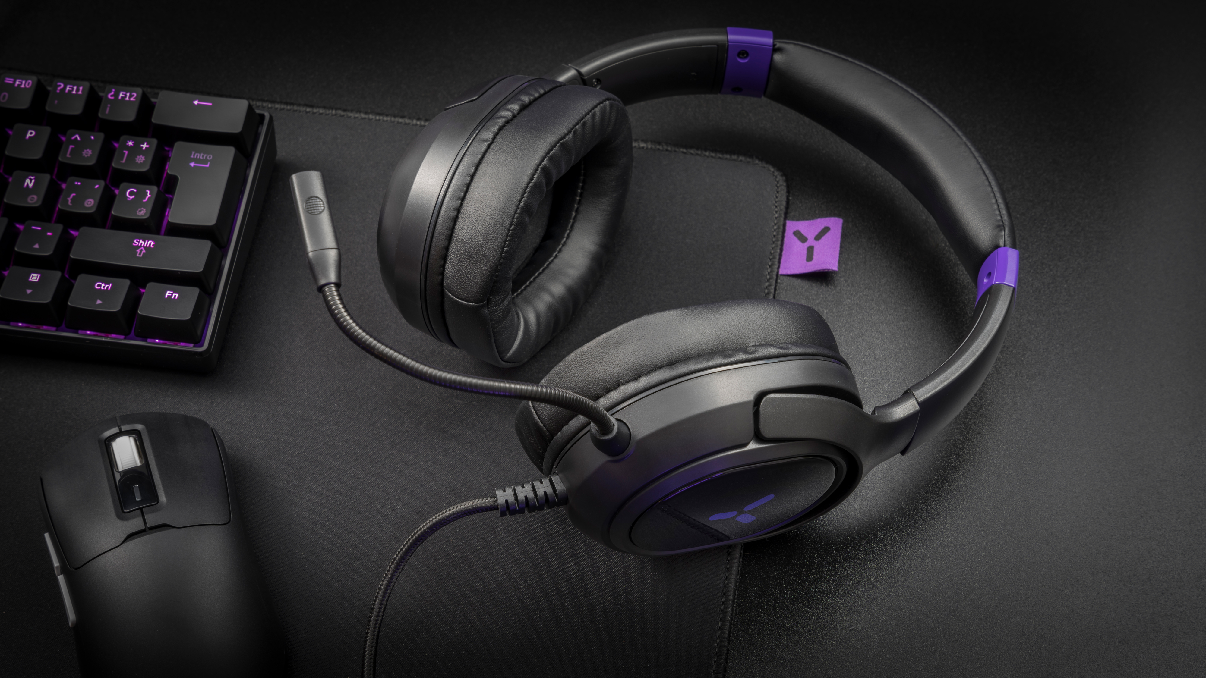 Schwarzes Gaming-Headset mit Mikrofon auf einem schwarzen Schreibtisch. Tastatur und Maus sind ebenfalls vorhanden.