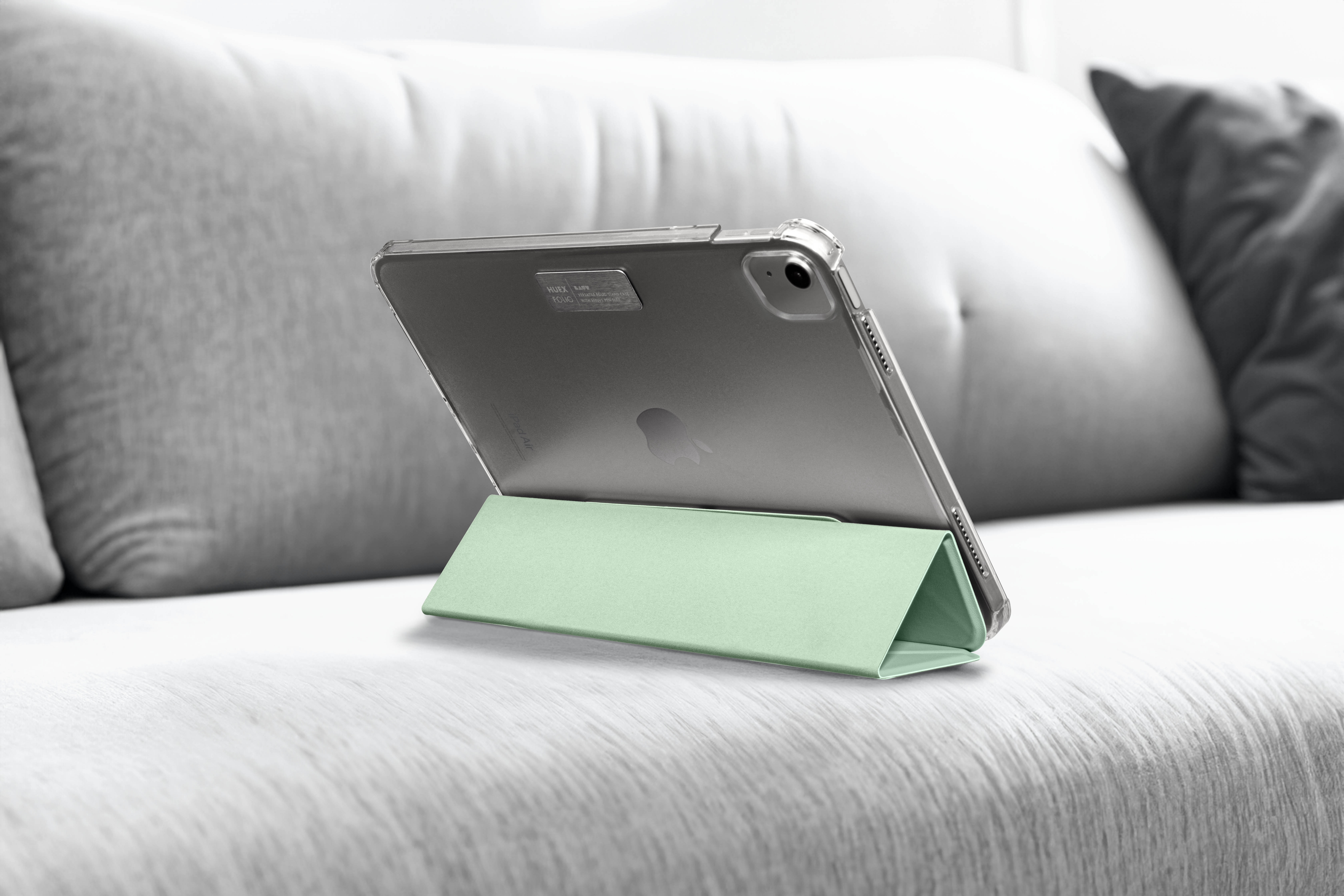 Tablet in einem grünen Ständer auf einem grauen Sofa. Das Tablet ist in einer transparenten Hülle.