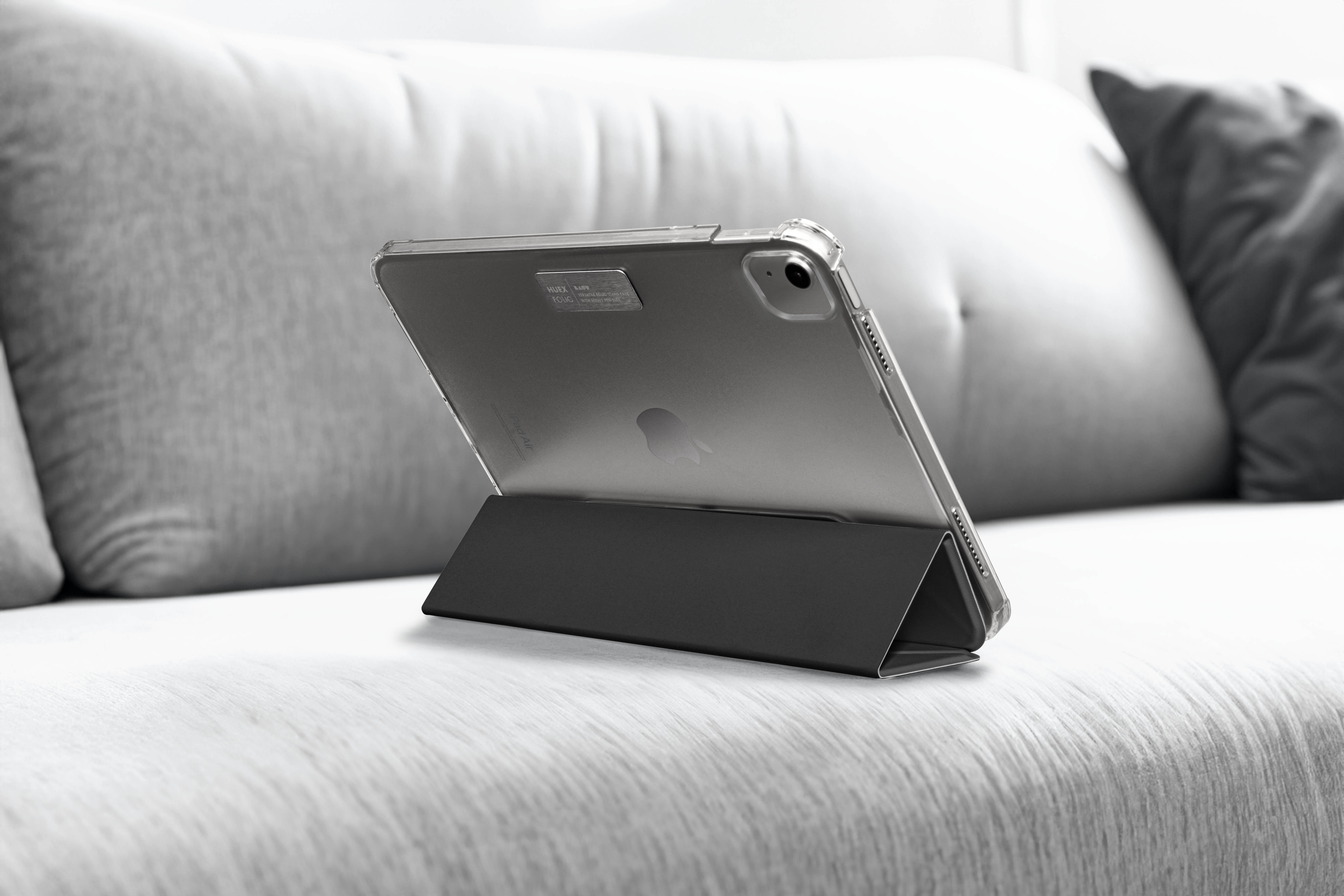 Ein iPad in einer durchsichtigen Hülle, auf einem schwarzen Ständer, auf einem grauen Sofa.