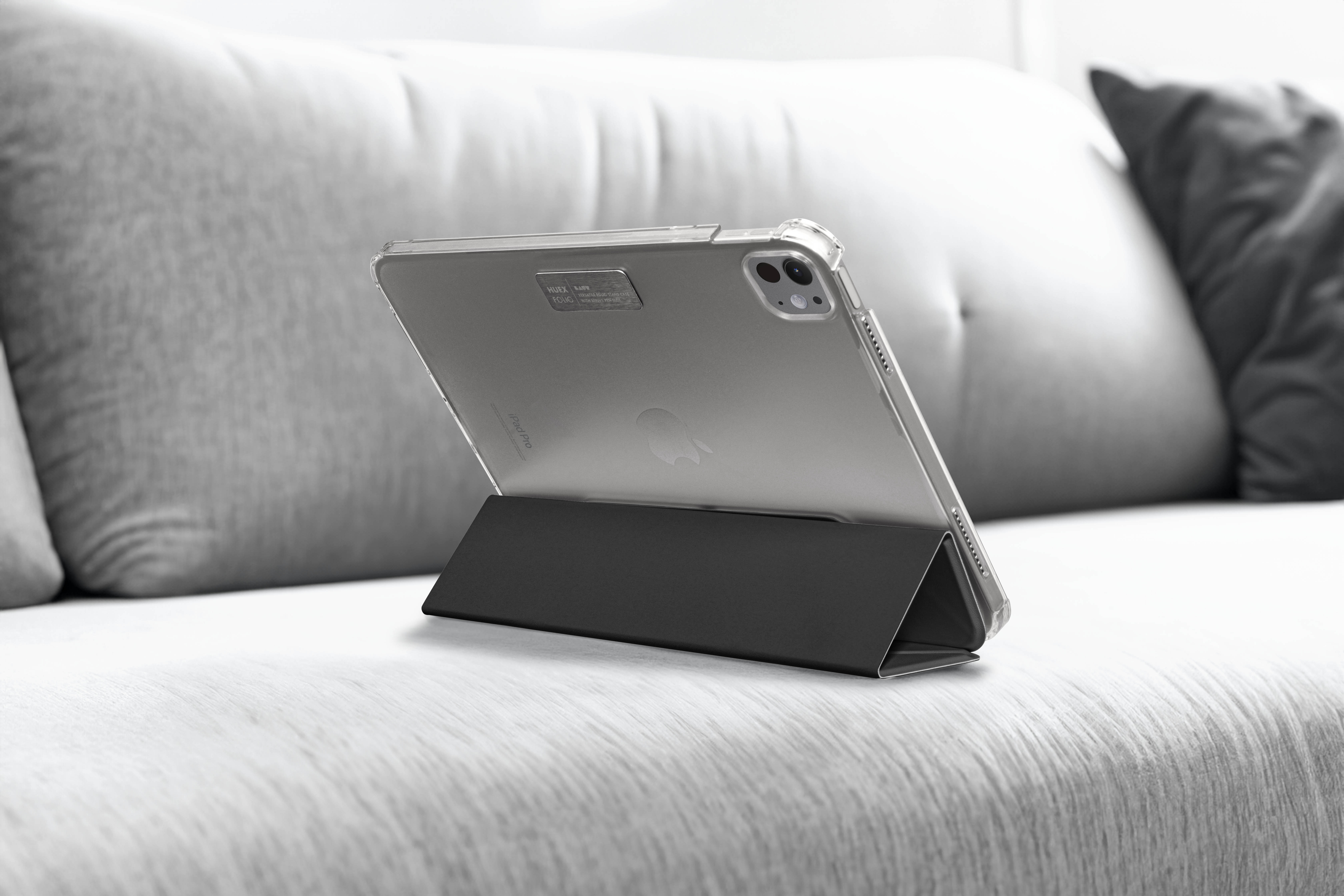 Un iPad posé sur un support gris foncé sur un canapé gris. L'iPad est dans un étui transparent.